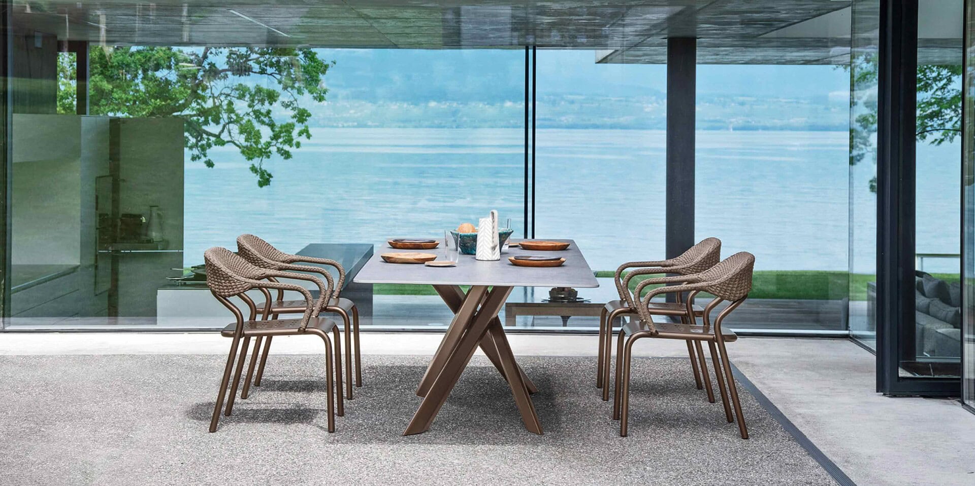 Stylish outdoor dining table with wicker chairs overlooking water, perfect for patio spaces.
