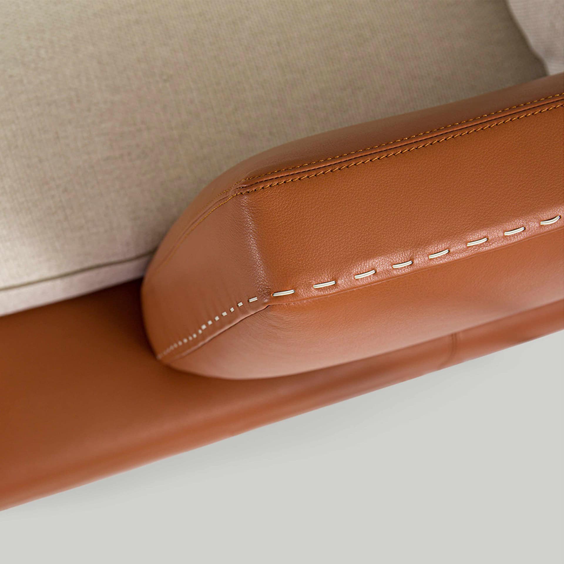 Luxurious caramel leather sofa armrest with detailed stitching, showcasing premium craftsmanship.