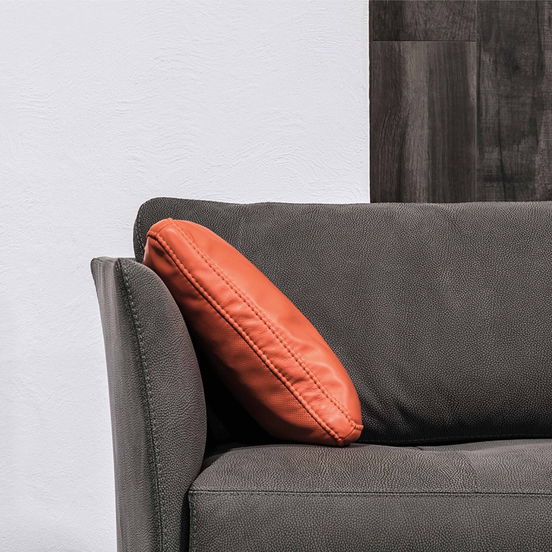 Modern grey sofa with orange accent pillow, stylish living room furniture design.