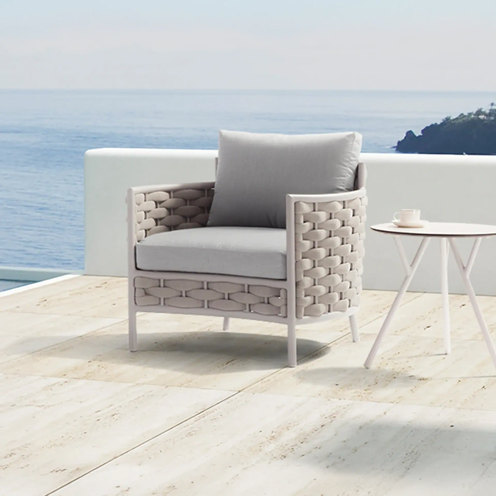 A modern outdoor armchair and side table on a tiled patio overlooking a blue sea and distant land.