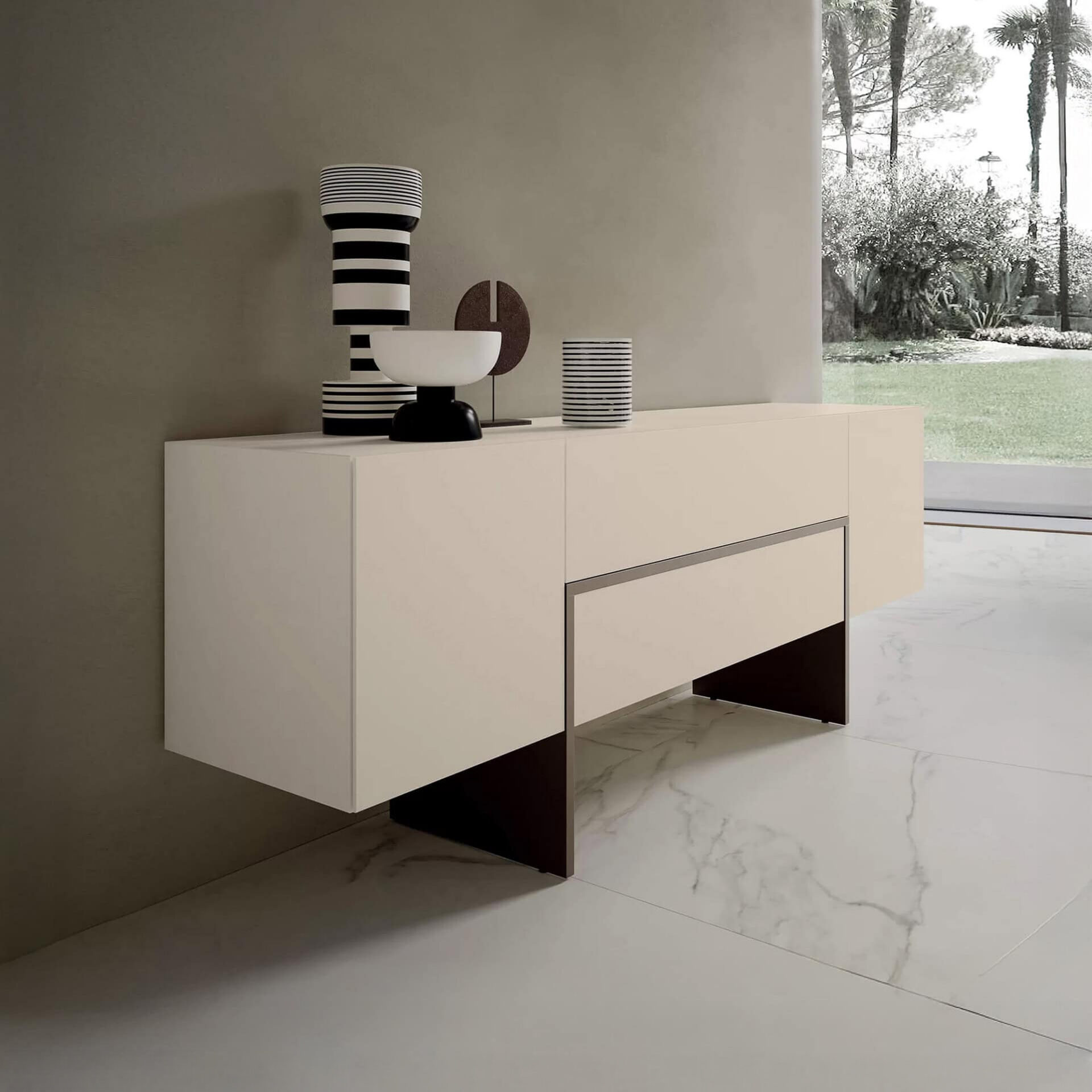 A modern light beige sideboard with black and white striped decor against a grey wall, overlooking a lush garden with palm trees through a large window.