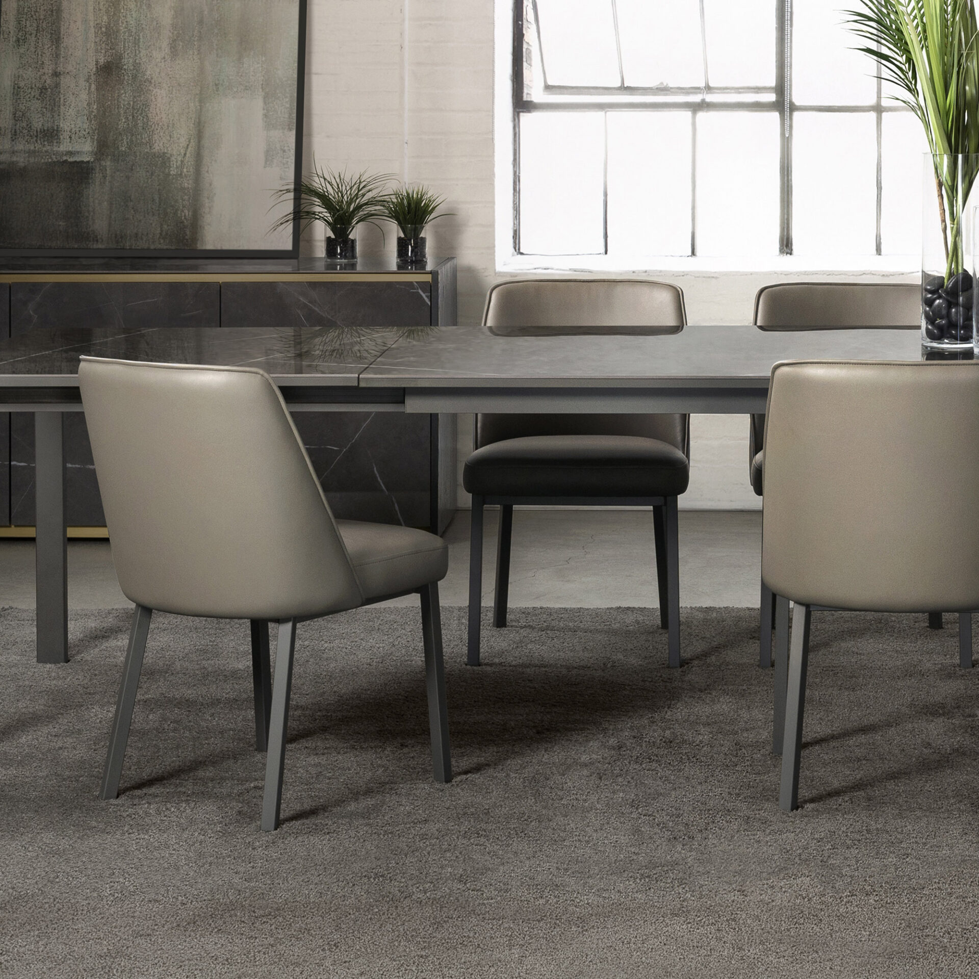 A modern dining room with a dark grey marble-effect table, light taupe chairs, a dark marble-patterned sideboard, and an industrial-style window.