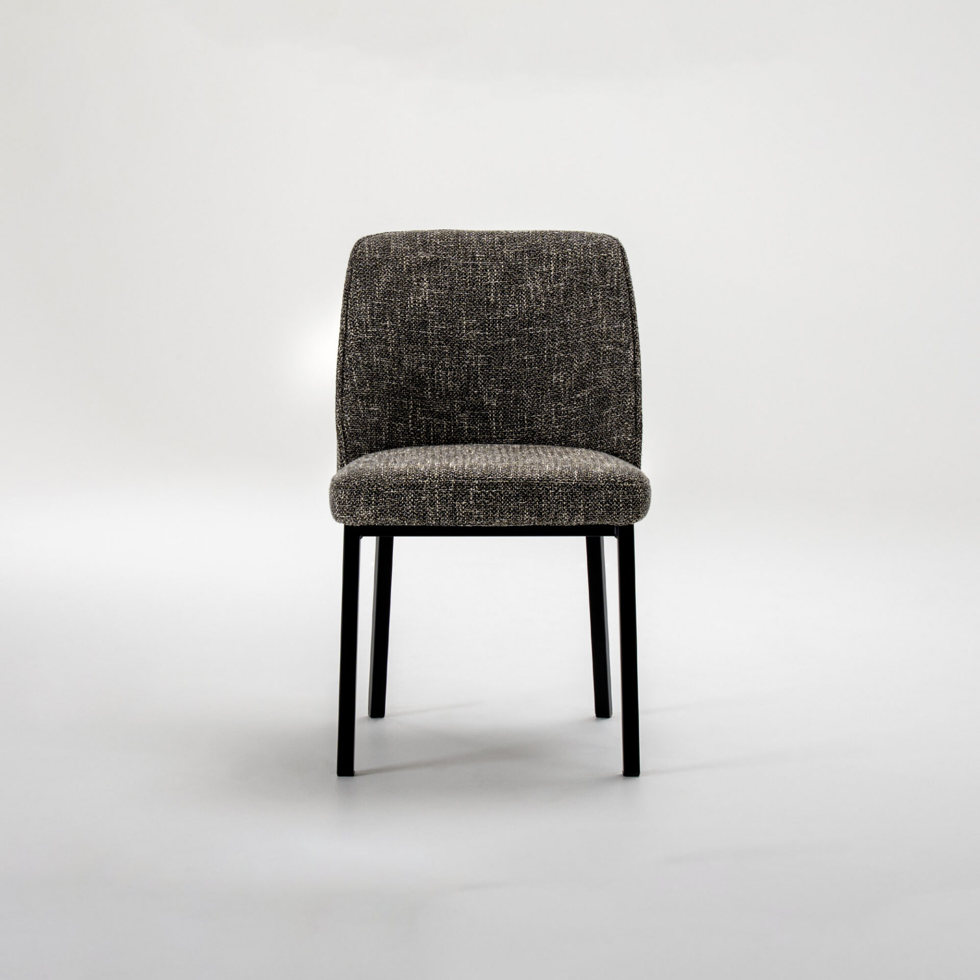 Front view of a modern dining chair with dark, textured grey and black upholstered seat and backrest, and slender black metal legs, against a white background.