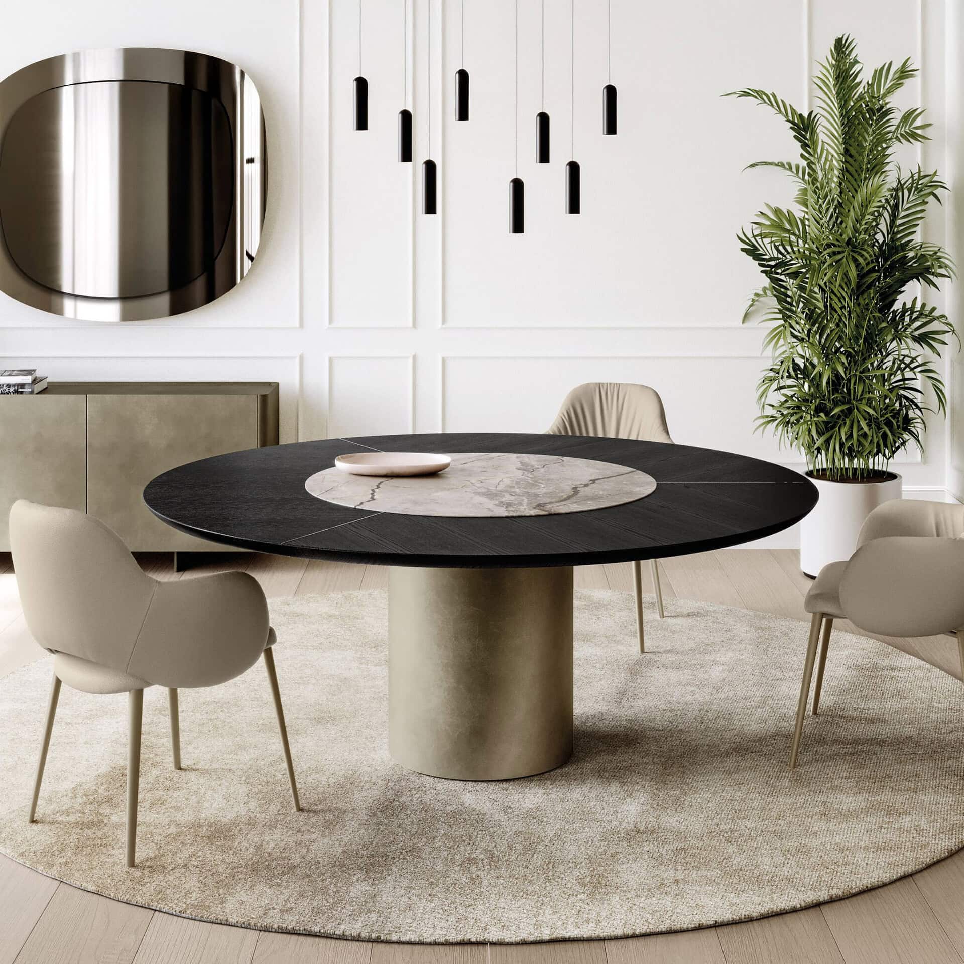 A modern dining room featuring a round dark wood and marble table, light beige upholstered chairs, a round beige rug, and a cluster of black pendant lights. A large metallic mirror and a green plant complete the sophisticated decor.