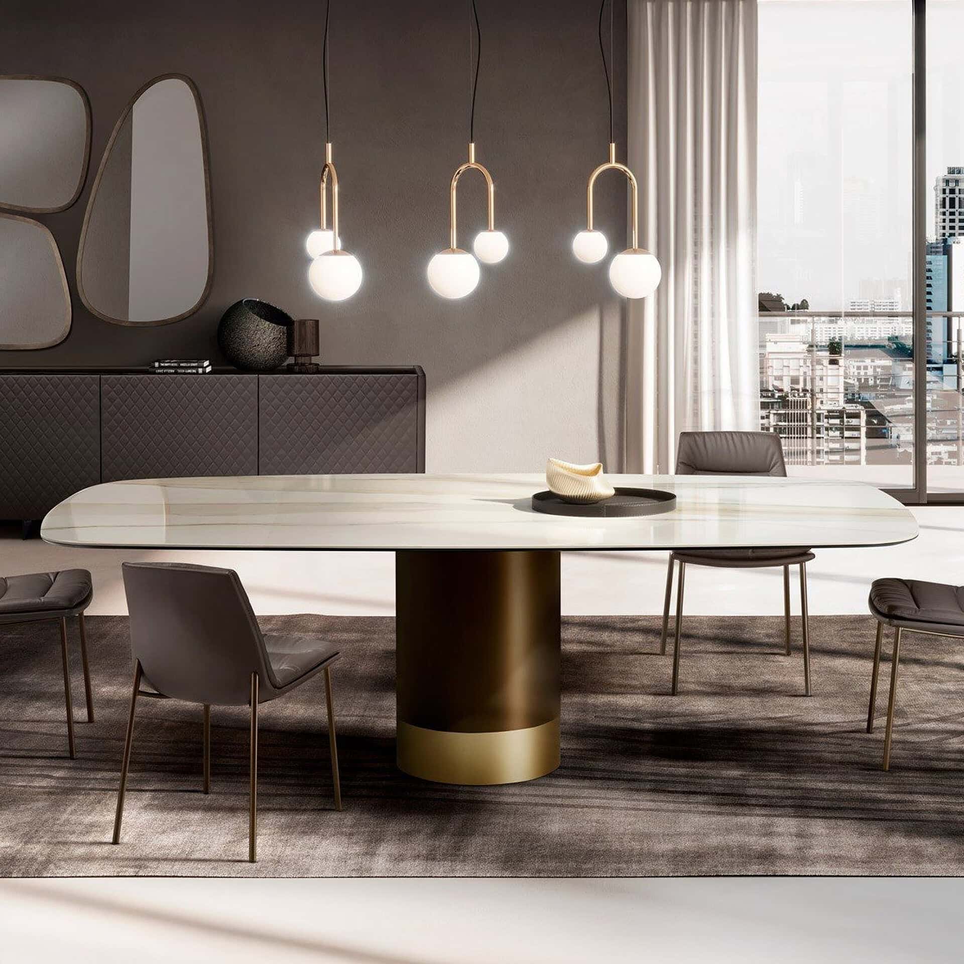 A modern dining room with an oval marble table, dark leather chairs, and gold globe pendant lights. A dark credenza with organic mirrors is in the background, and a city skyline is visible through a large window.