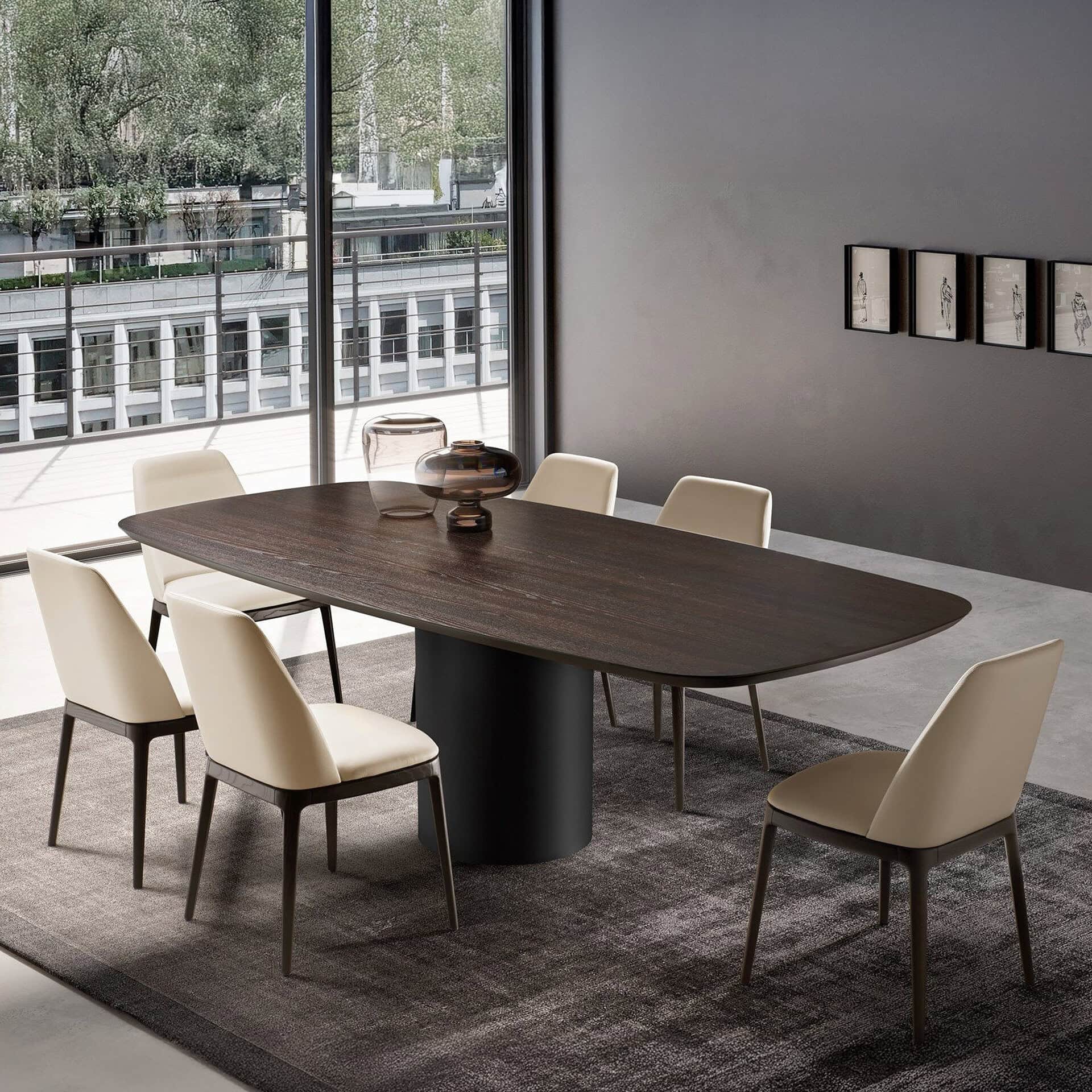 A modern dining room with a dark wood oval table, six cream upholstered chairs, and a large window revealing an urban city view with trees and buildings. A dark grey wall with framed art is on the right.