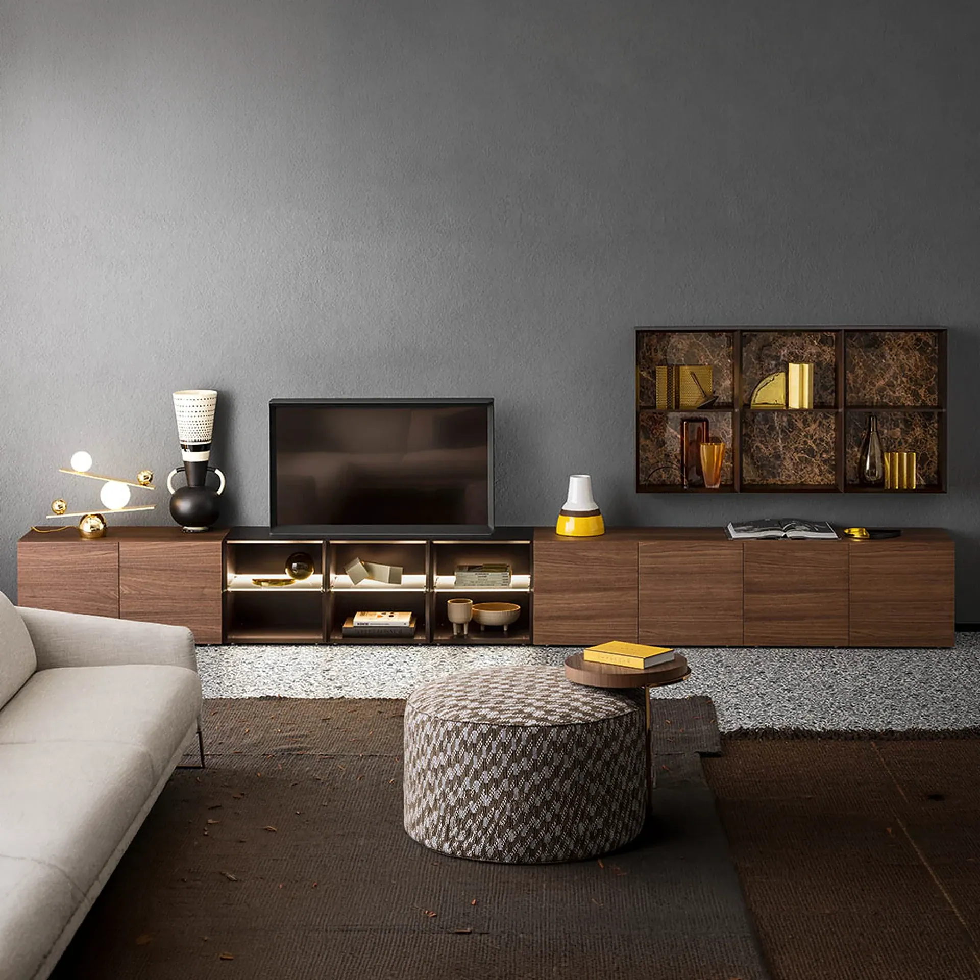 A modern living room with a dark wood media console, flat-screen TV, decorative objects, and a patterned ottoman on a layered rug.