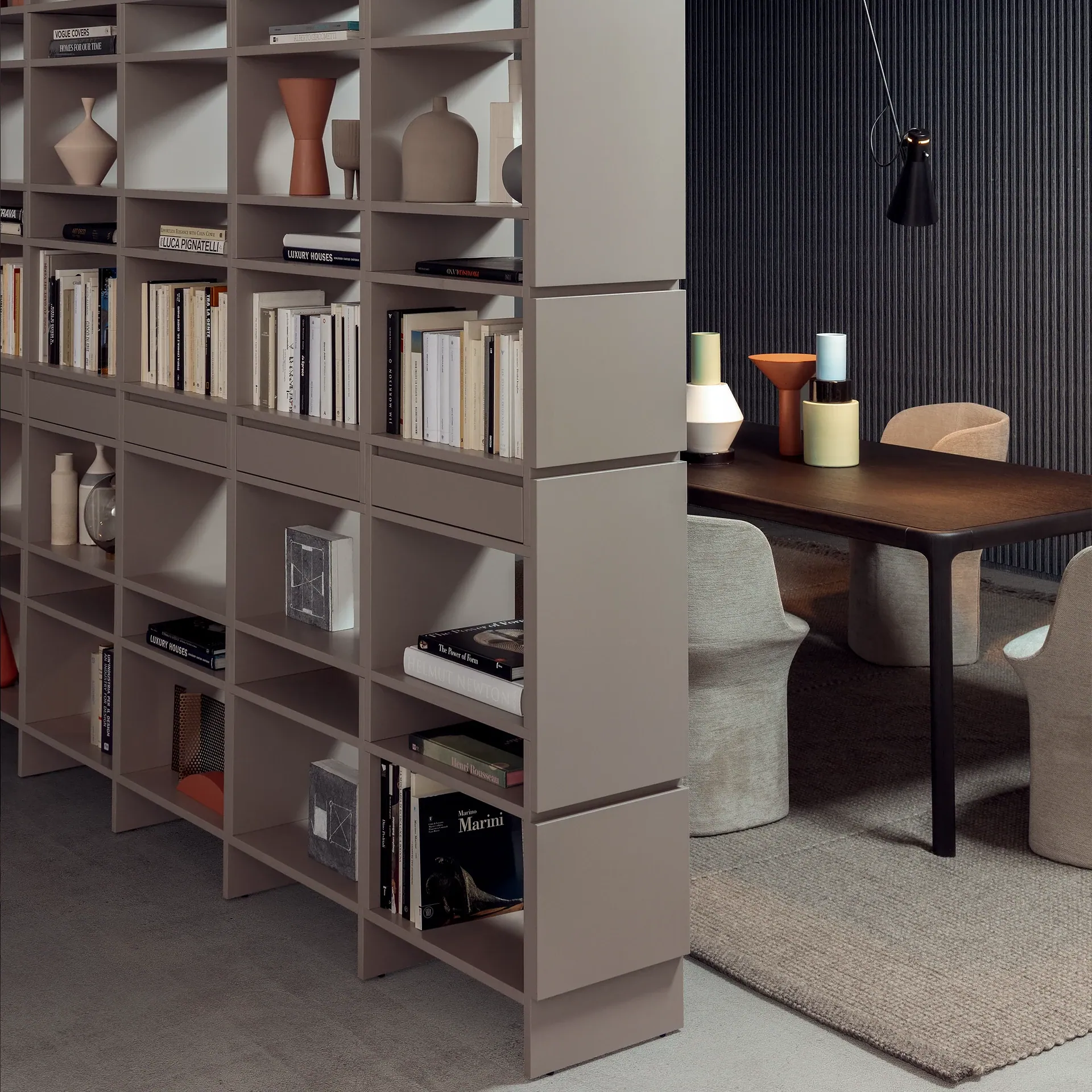 Modular bookshelf with open cubbies and decorative ceramic vases near a dark wood dining table.