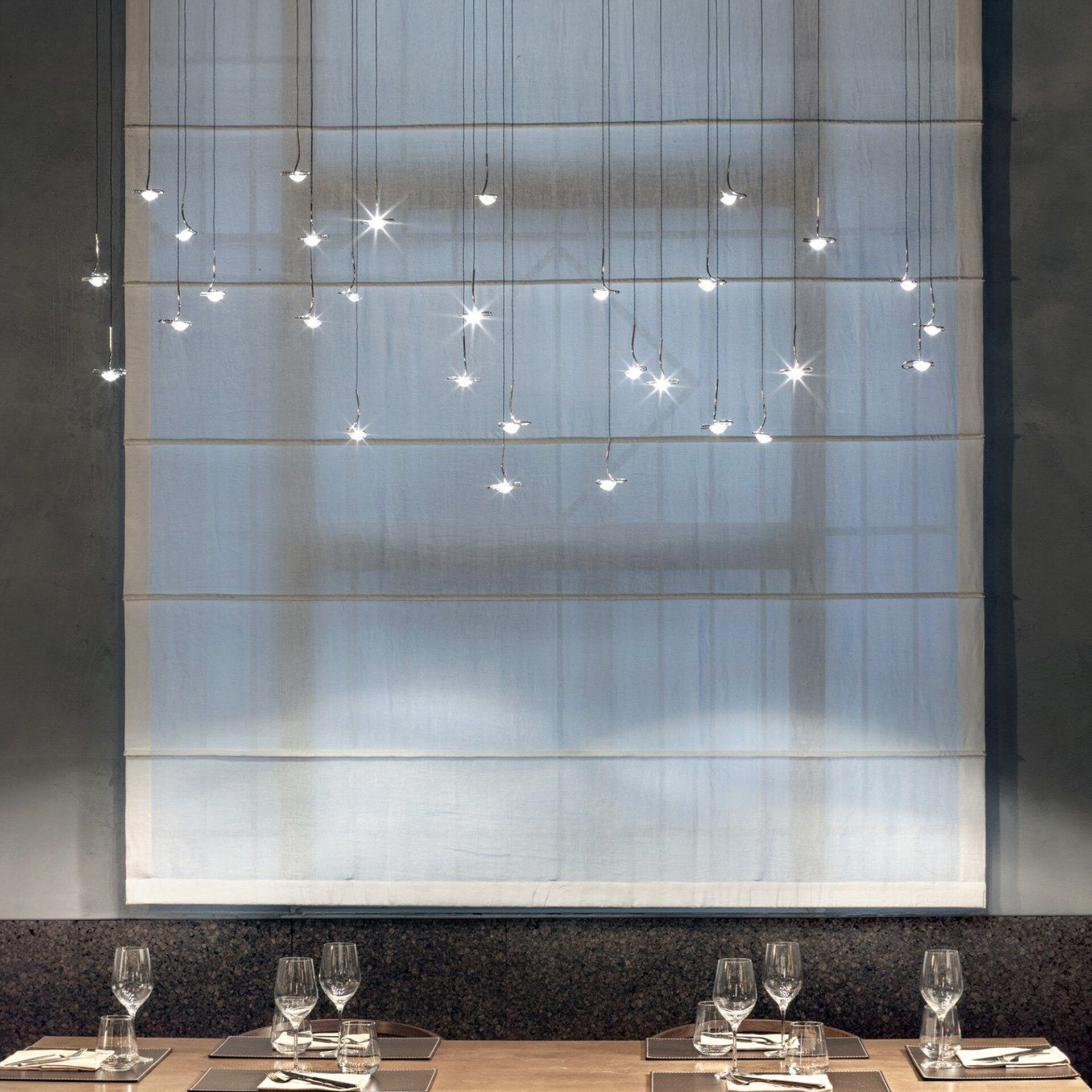 Jackie O Sculptural Glass LED Chandelier hanging in front of large windows, showing the airy suspension and floating glass pendants in a modern interior.