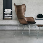 Sleek modern designer lounge chair and matching ottoman with wooden finish and metal legs in contemporary home setting.