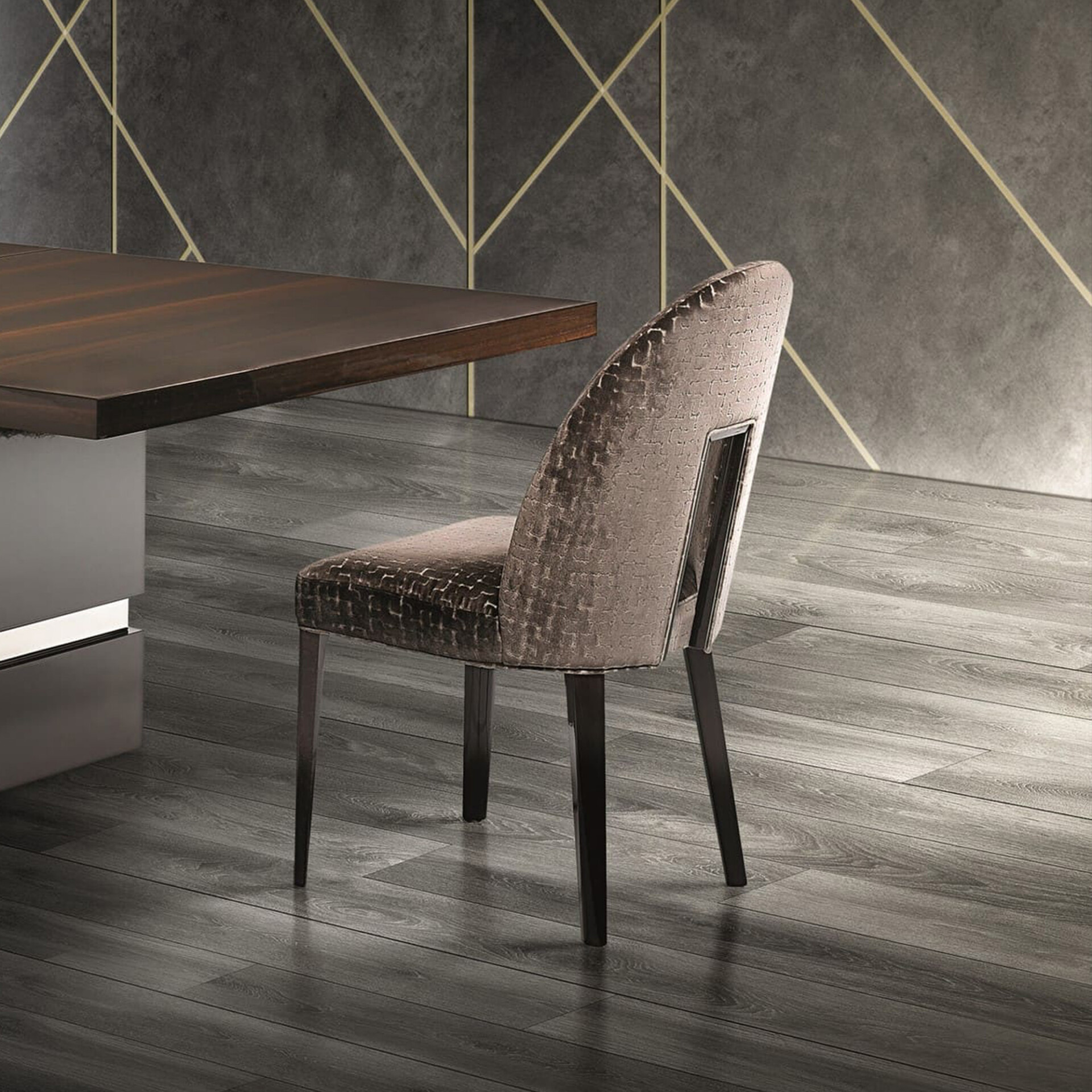 Luxurious taupe dining chair with textured fabric and metallic detail, next to a dark wood table. Dark grey wall with gold geometric lines and dark wood floor.