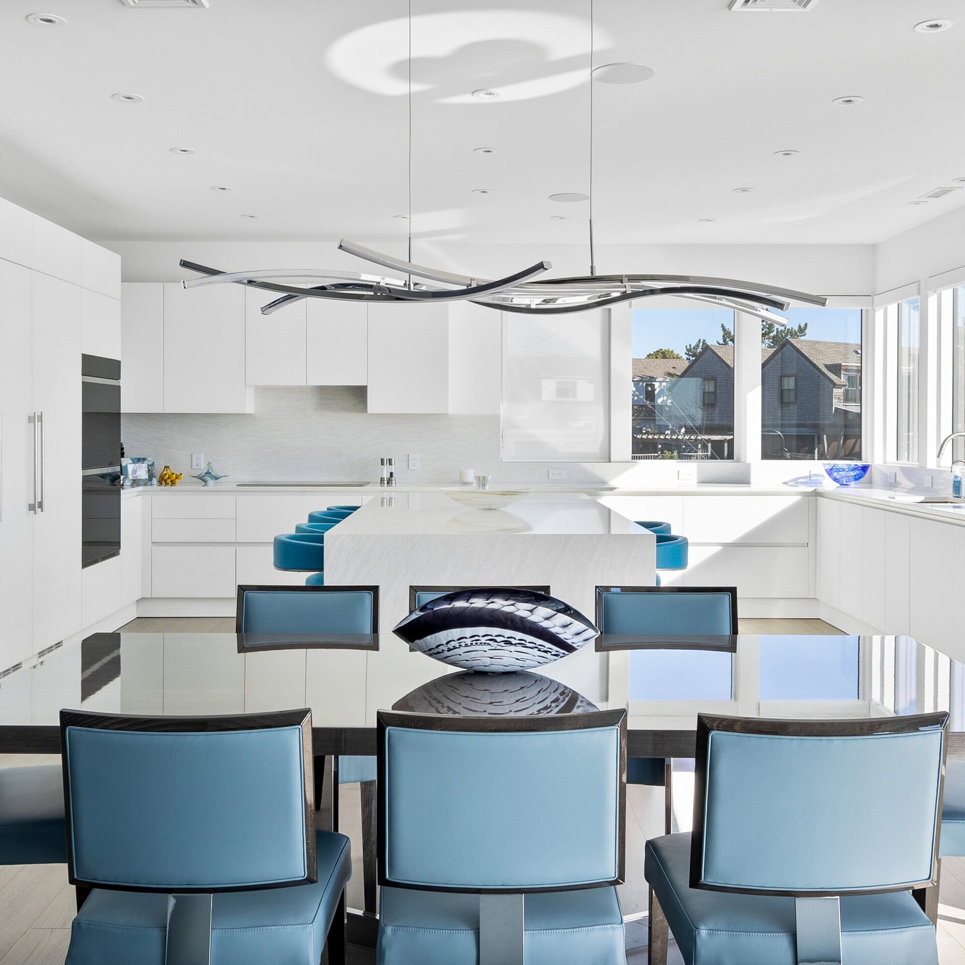 Contemporary white kitchen with blue upholstered dining chairs and modern chandelier, stylish and functional design.