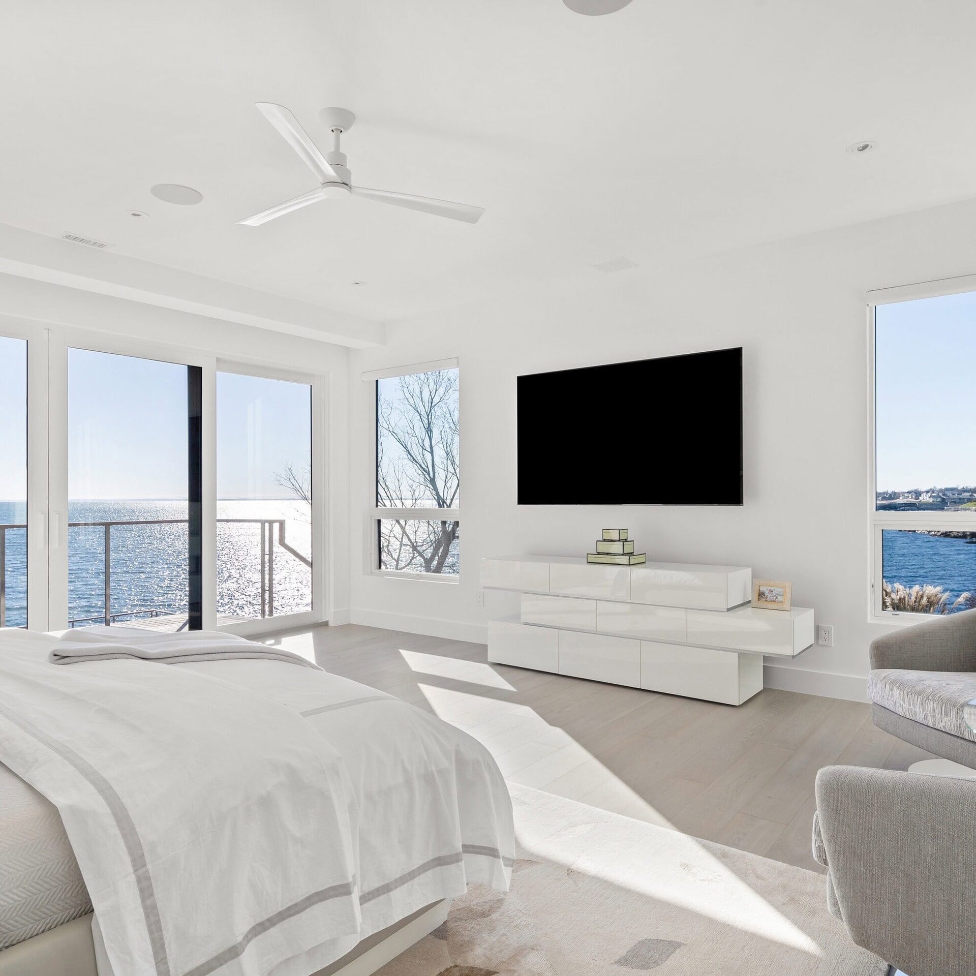 Bright modern bedroom with sea view, minimalist white decor, and sleek entertainment setup.