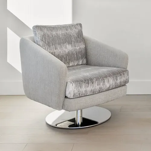 A light gray barrel swivel armchair with a patterned seat cushion and throw pillow, on a chrome base, in a modern room with light walls and wood floor.