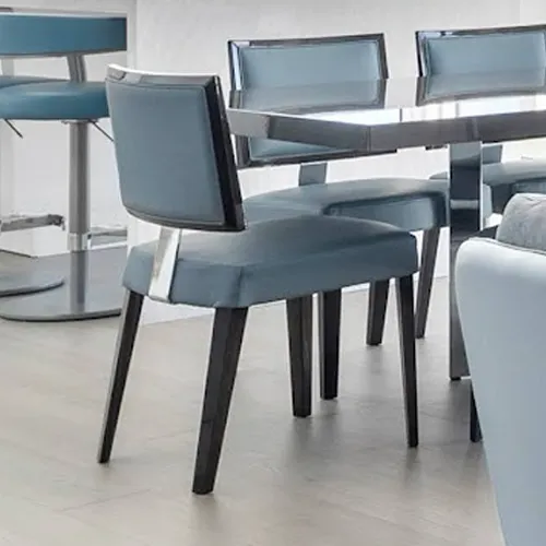 Modern dining chair with blue upholstery and dark legs, next to a dining table and a blue bar stool on light wood flooring.