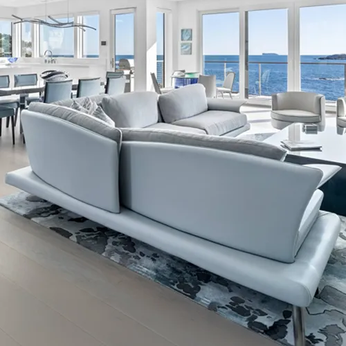 A modern living room with a light blue sectional sofa overlooking a panoramic ocean view through large windows.