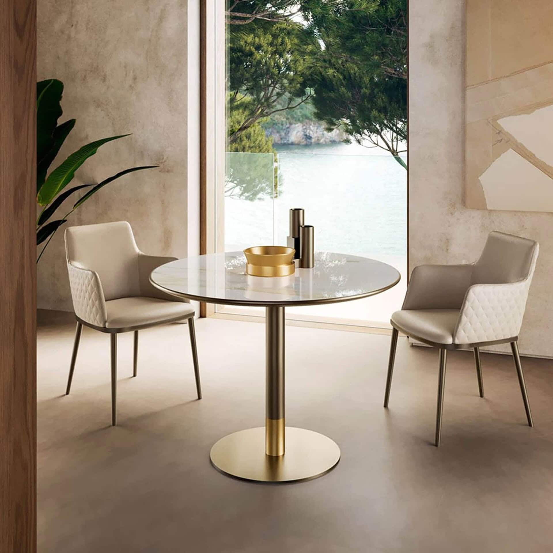 Cilindro Bistro Table with gold base and round ceramic top styled in a modern dining setting.