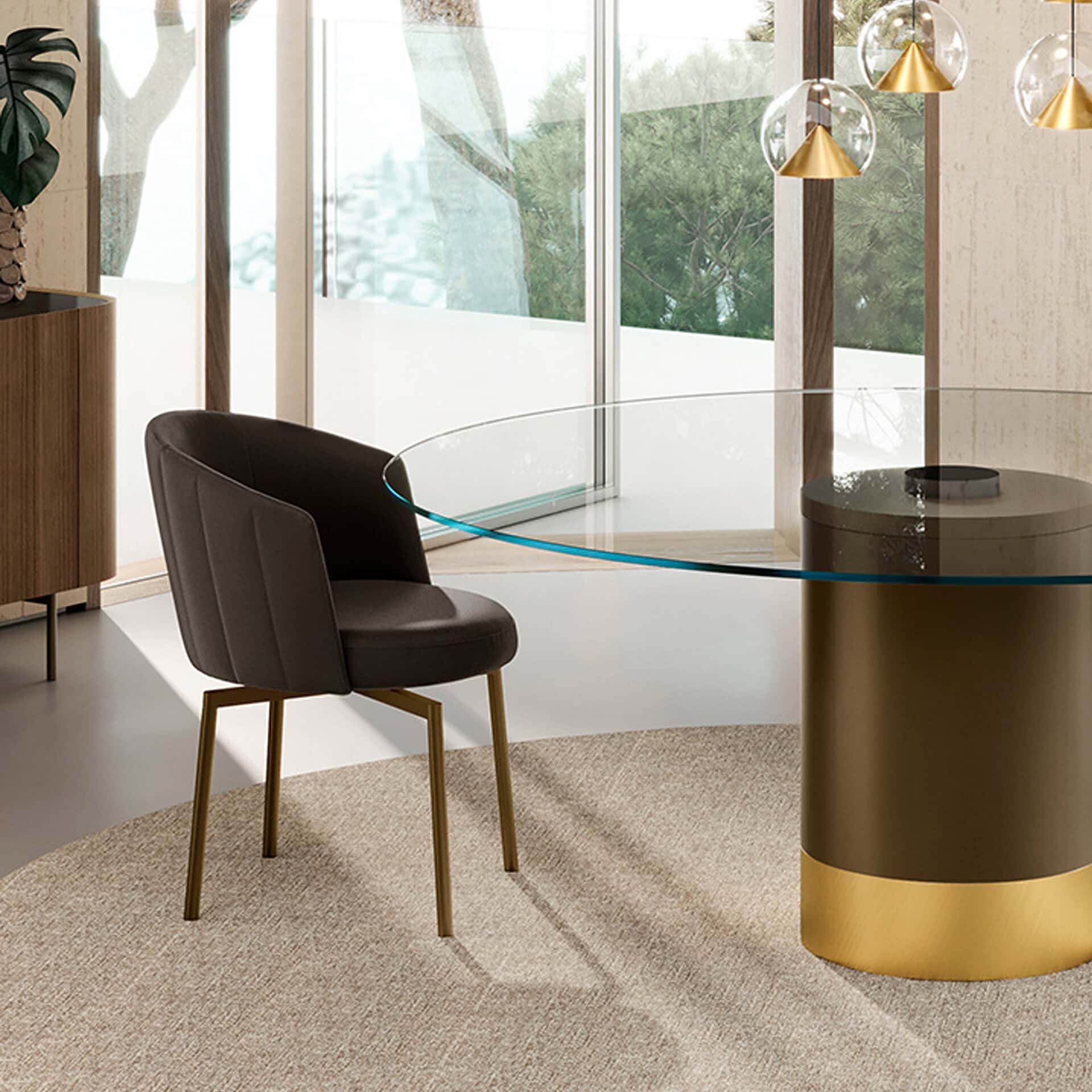 A modern dining area with a round glass table, dark brown ribbed chair with gold legs, and three spherical pendant lights, all set on a beige rug in front of large windows overlooking green trees.