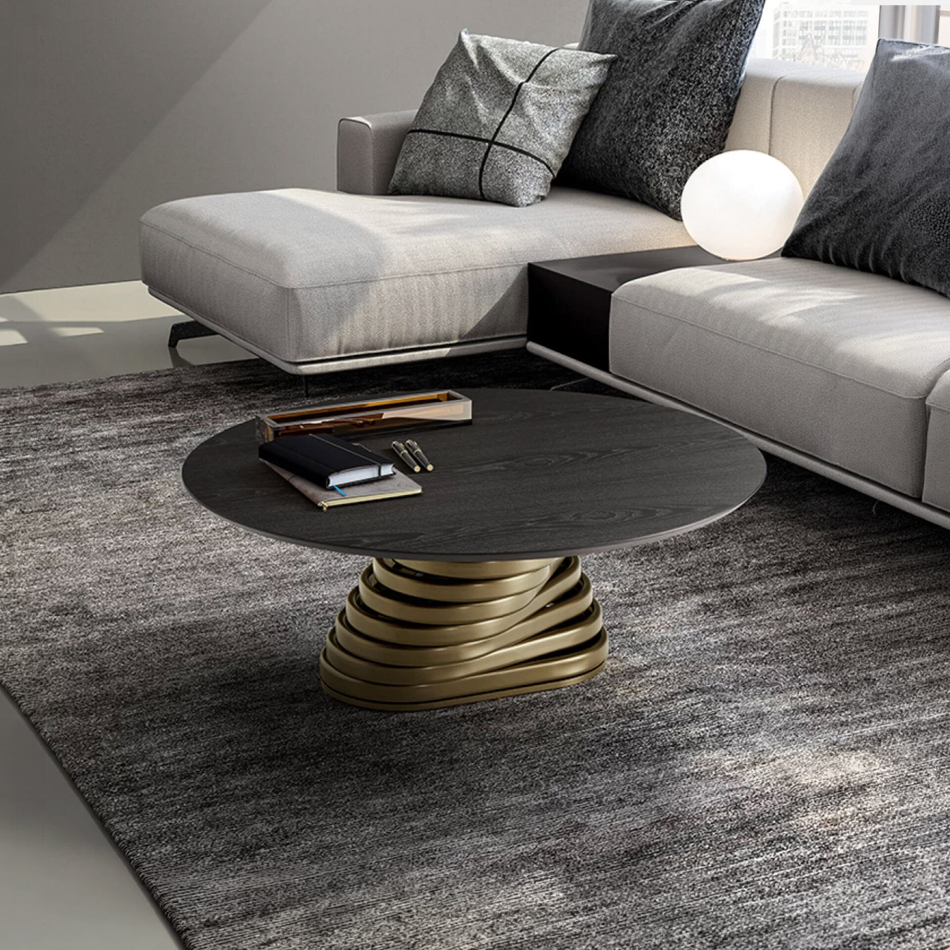 A modern living room featuring a round dark wood coffee table with a sculptural gold base, a light grey modular sofa with grey pillows, and a dark grey textured rug. A white spherical lamp sits on the sofa's side table.