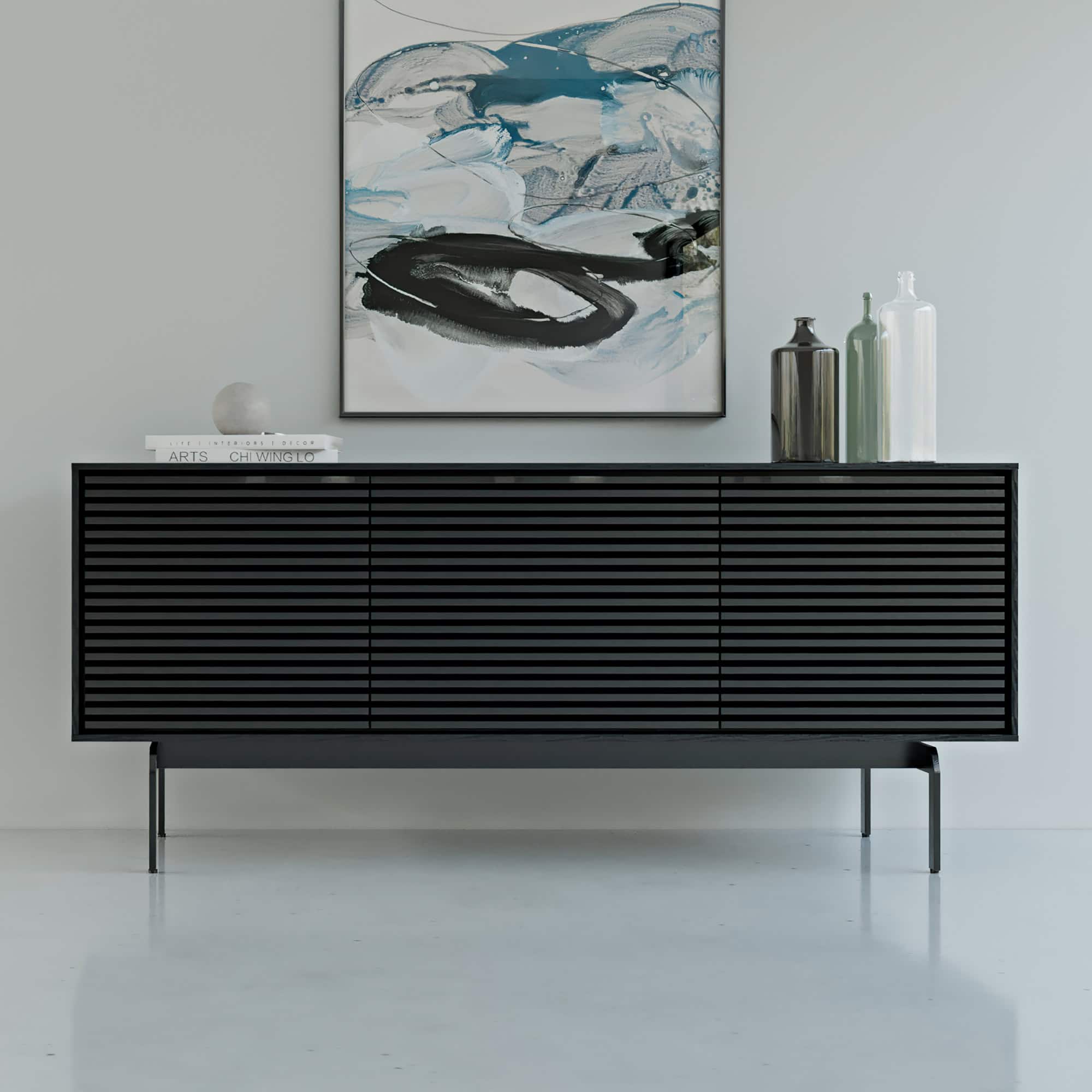 Black BDI Align 7477 media console with louvered doors styled with modern artwork.