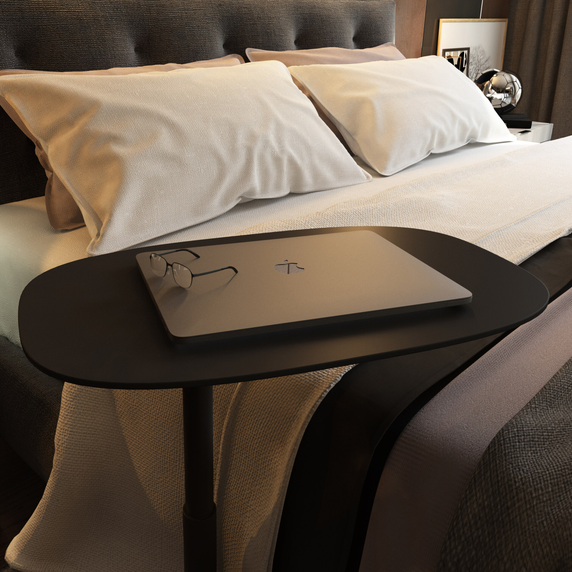 A modern bedroom with a dark upholstered bed, light beige bedding, and a black oval side table holding a silver laptop and dark-rimmed glasses.