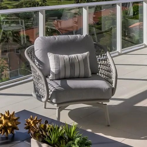 A modern gray outdoor armchair with a striped pillow on a tiled balcony, overlooking a green landscape and distant buildings through a glass railing.