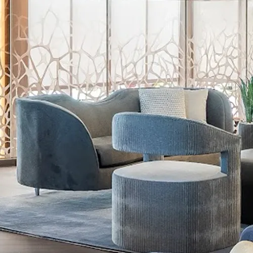 A blue velvet sofa and a blue ribbed armchair on a blue rug, with patterned window screens in the background.