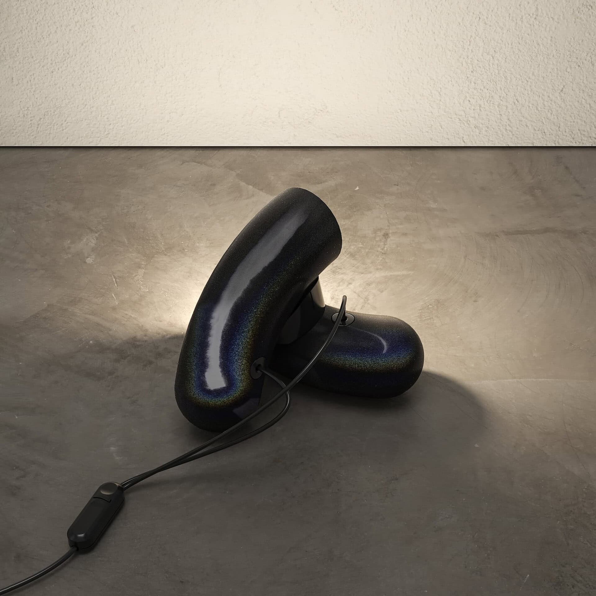 Sculptural black table lamp with a glossy, abstract design on concrete floor, modern home decor.