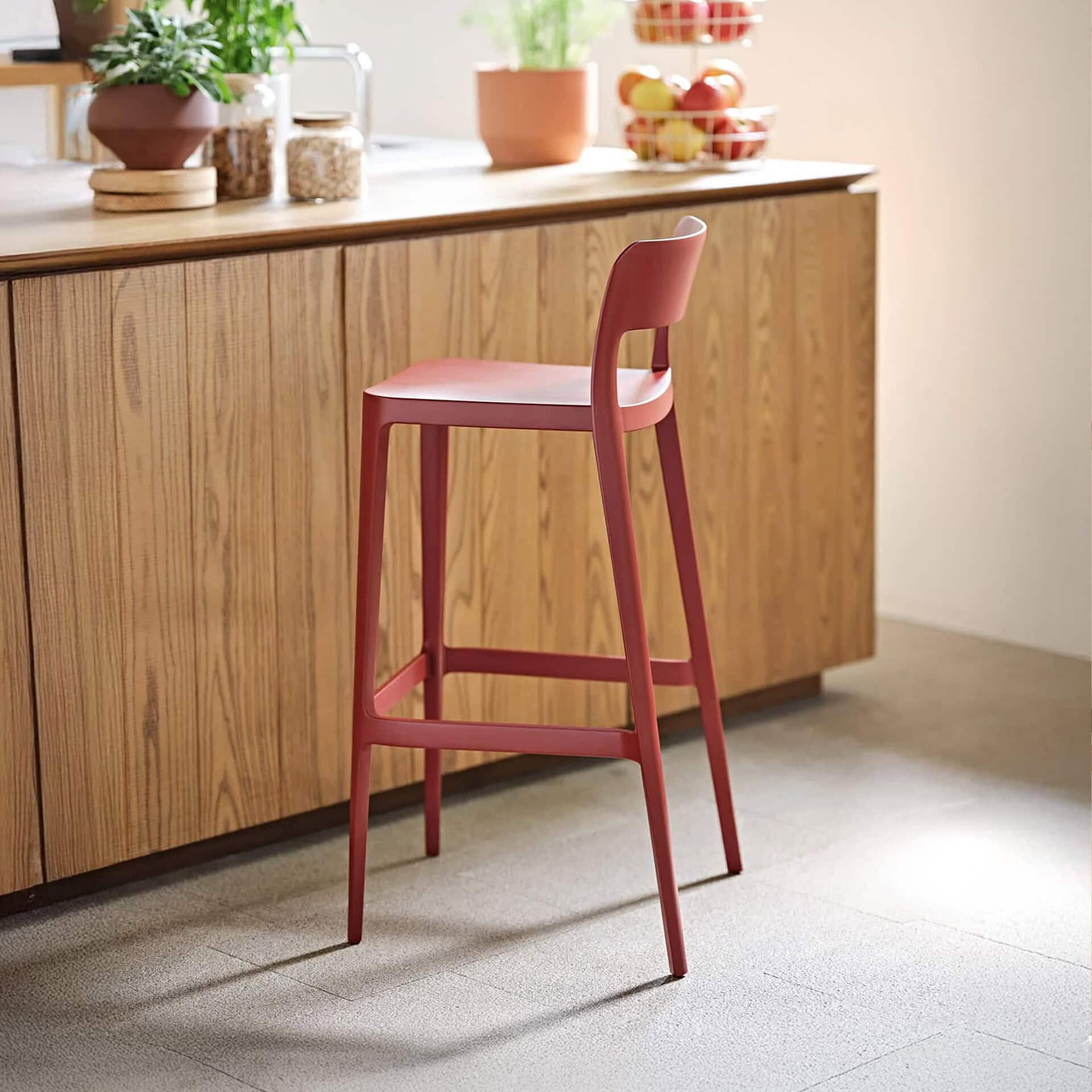 Nené stool in red polypropylene shown in a modern kitchen setting with wood cabinetry.