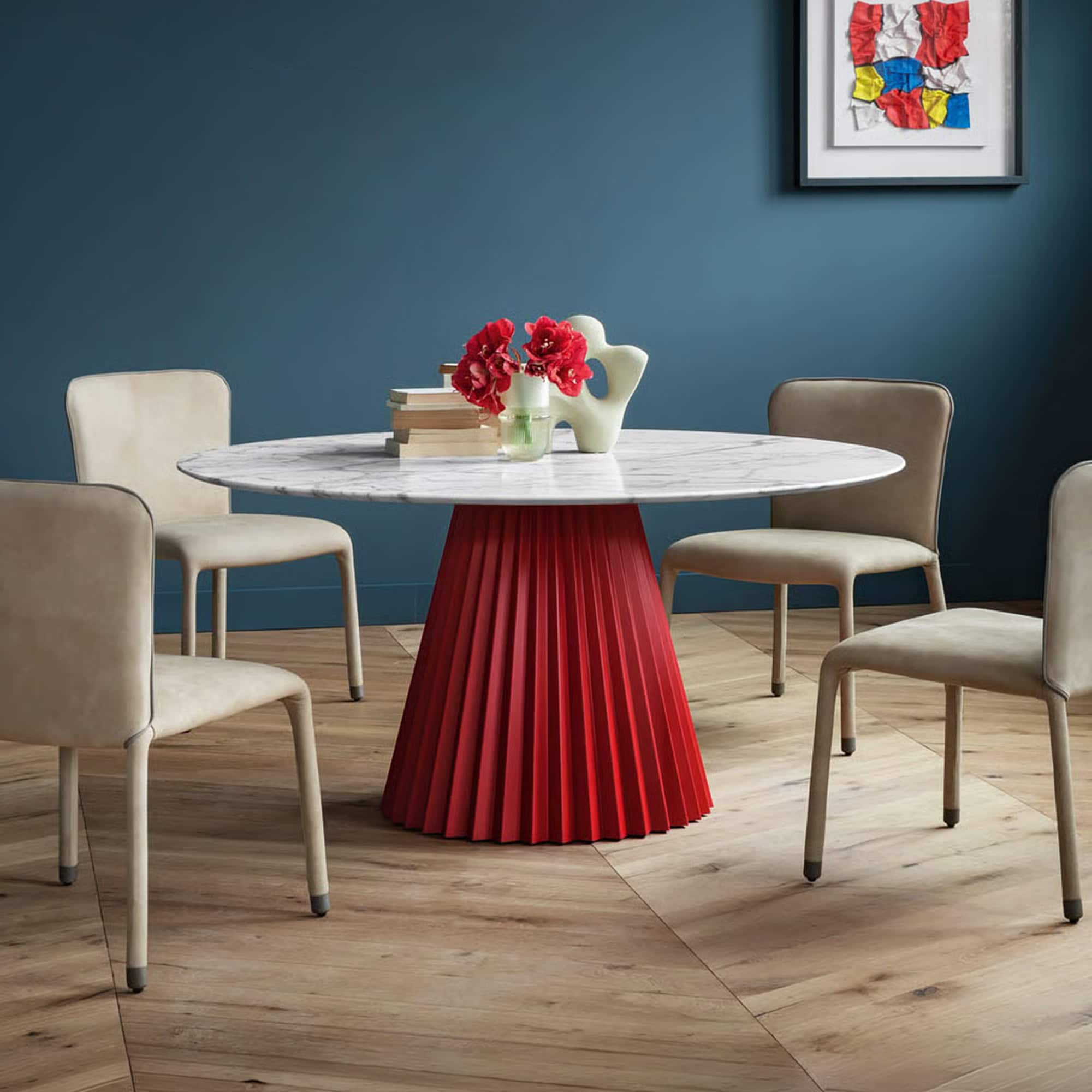 Modern round dining table with a red plissé base and marble top.