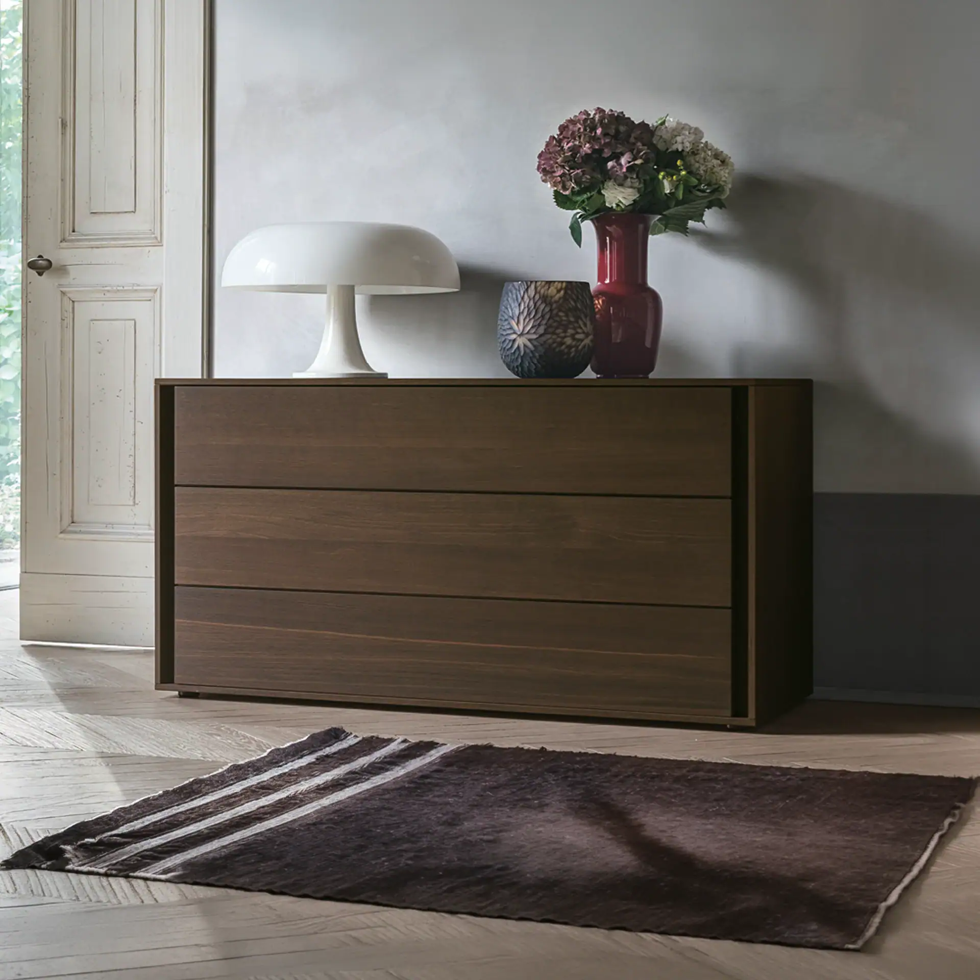 Modern wooden dresser with decorative vases and a lamp in a stylish interior setting.
