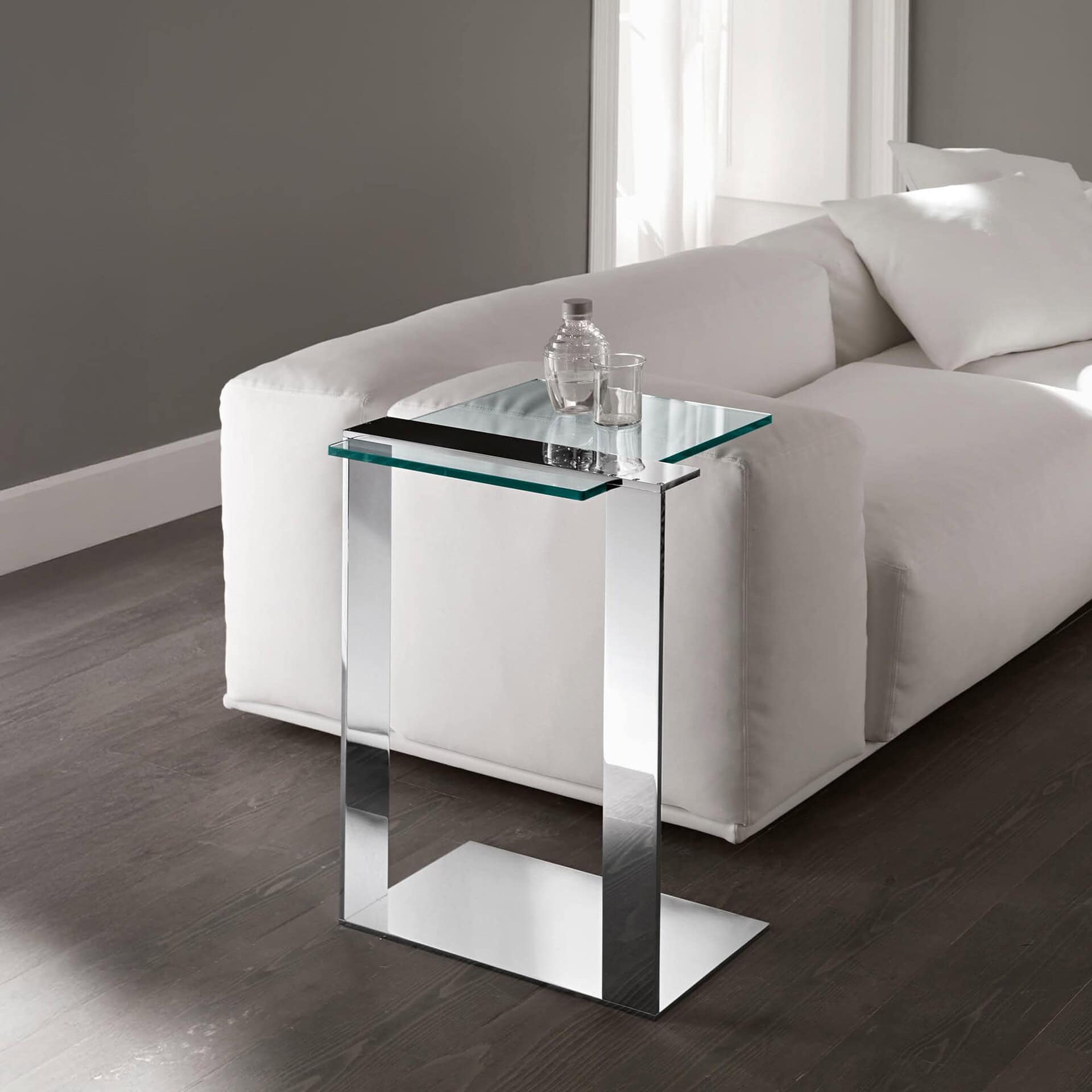 Chrome Joliet Side Table with transparent glass top, styled next to a white sofa in a contemporary living room.