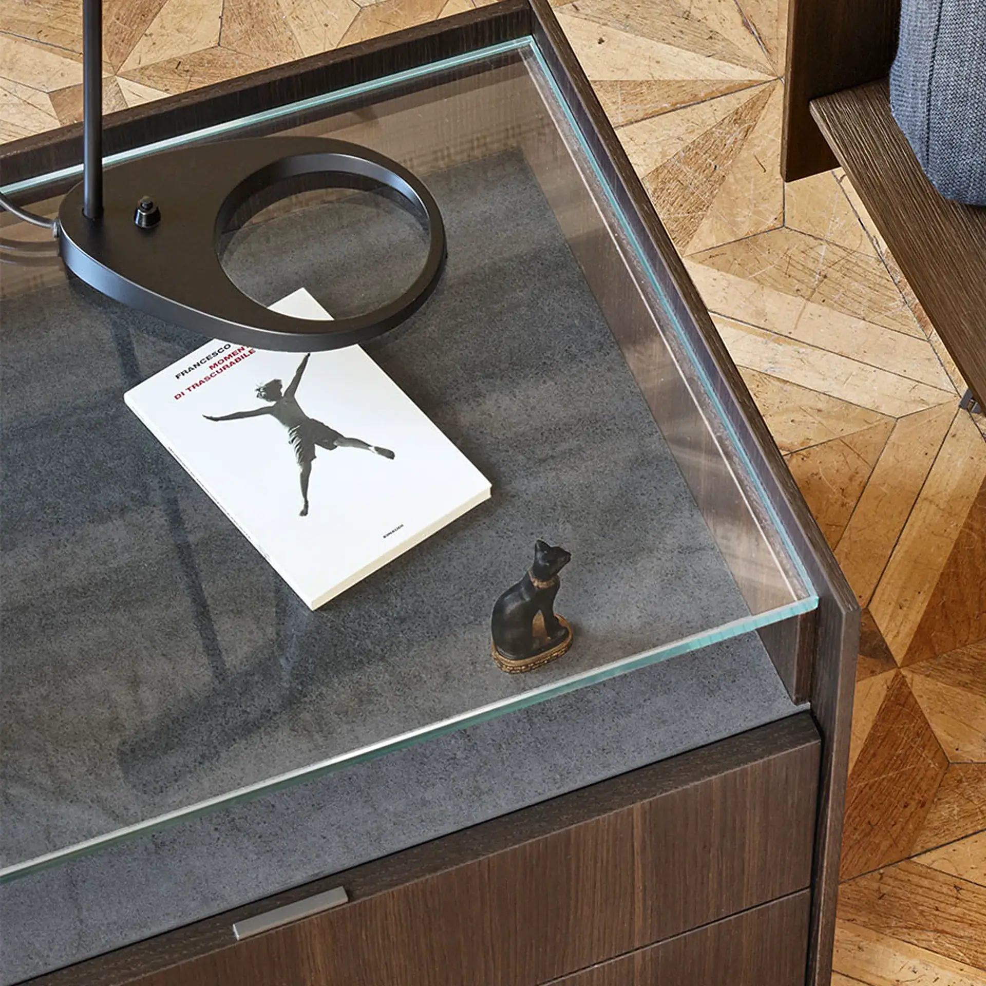 Elegant glass-topped display table with wooden base showcasing a magazine and decorative figurine.