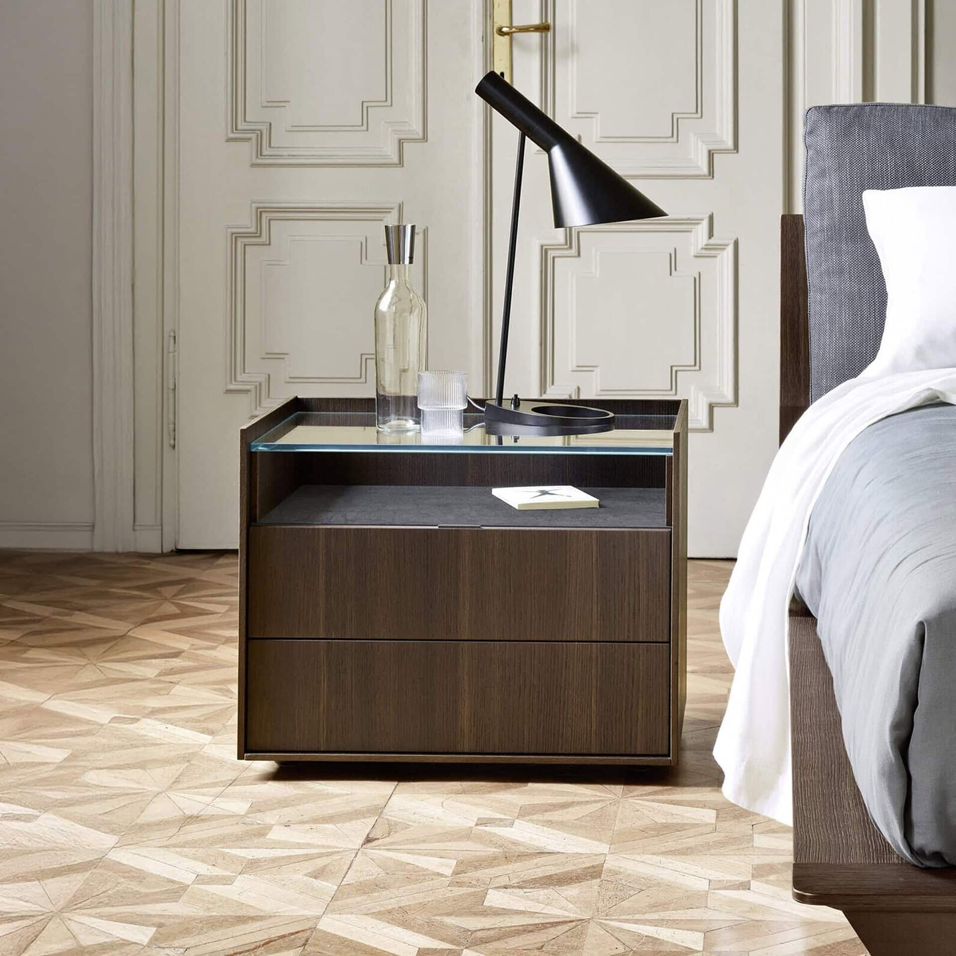 San Giacomo Cabaret Glass Nightstand in wood finish with glass top, styled beside modern bed