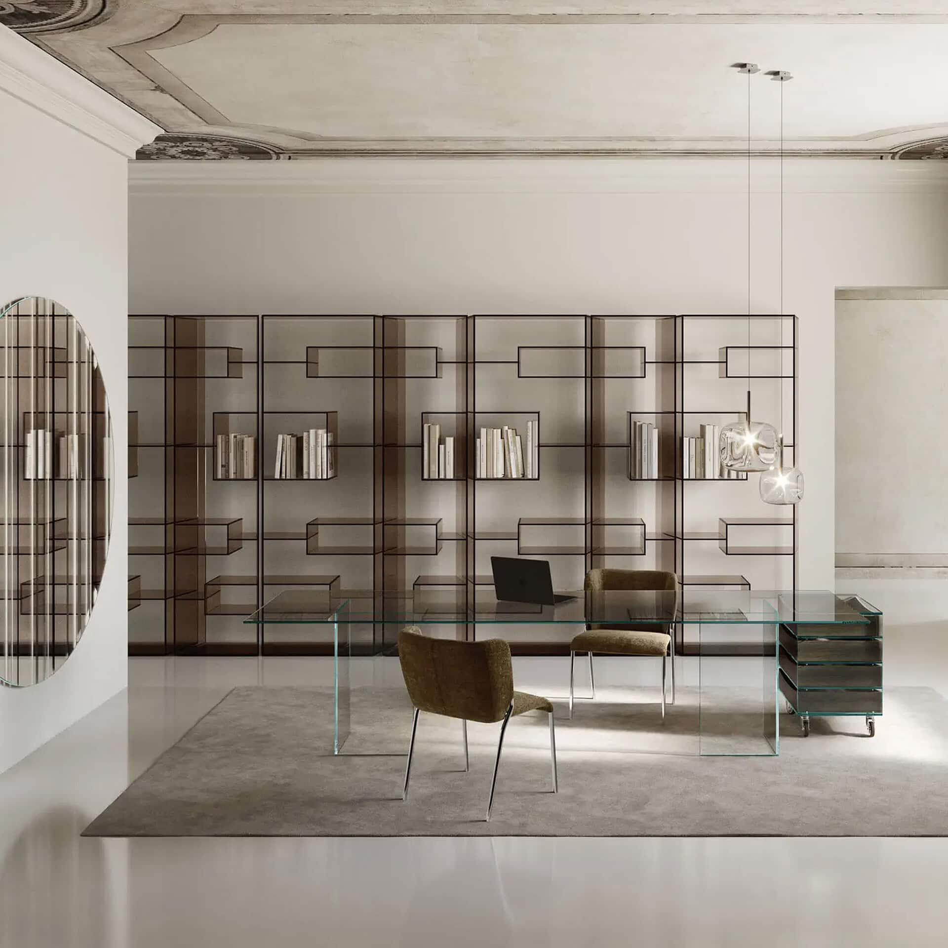A modern home office with a clear glass desk, two upholstered chairs, and a large modular bookcase, set in a room with an ornate classical ceiling and a large oval mirror.