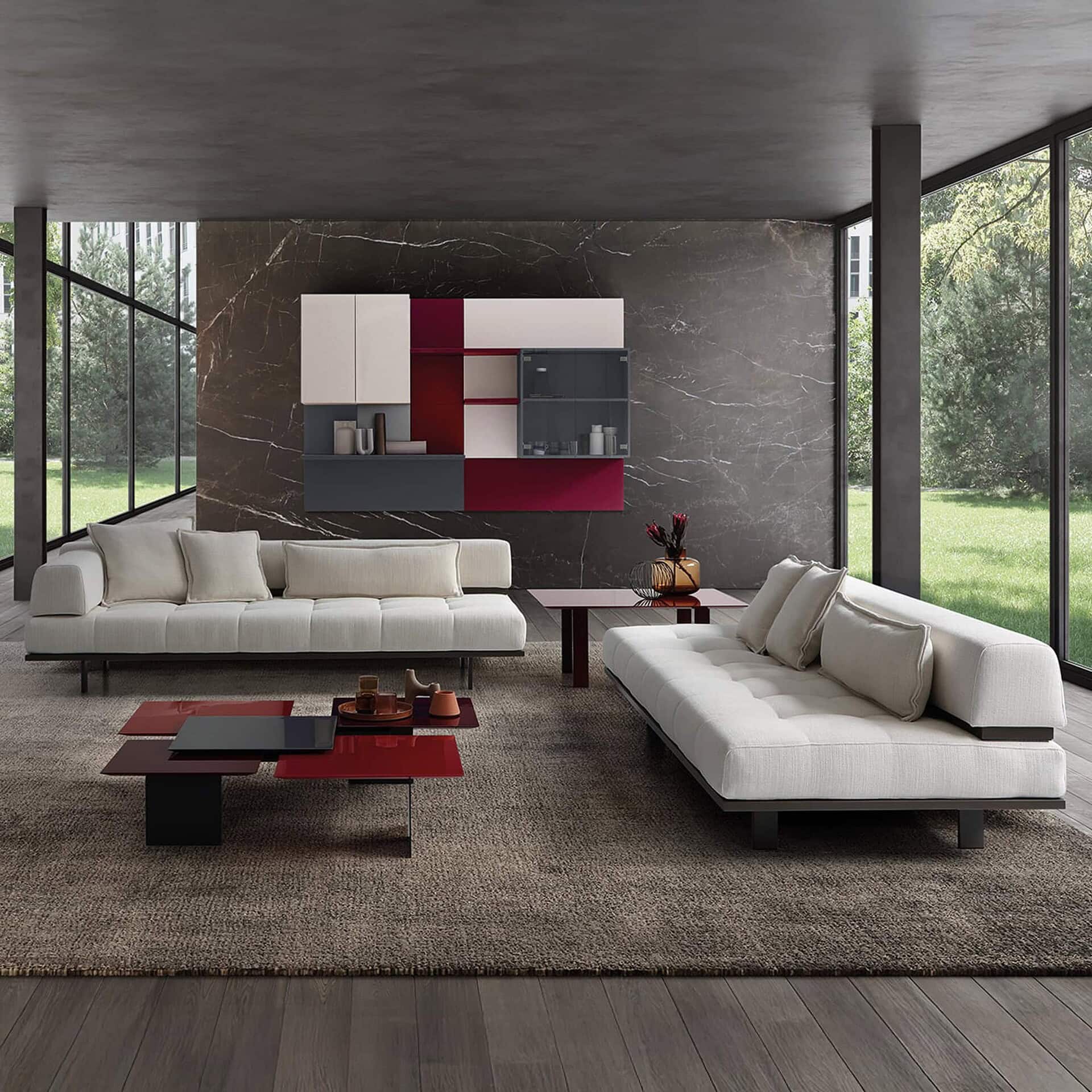 Modern living room with sleek white sofas, bold red, black, and white storage walls, and floor-to-ceiling windows overlooking greenery.