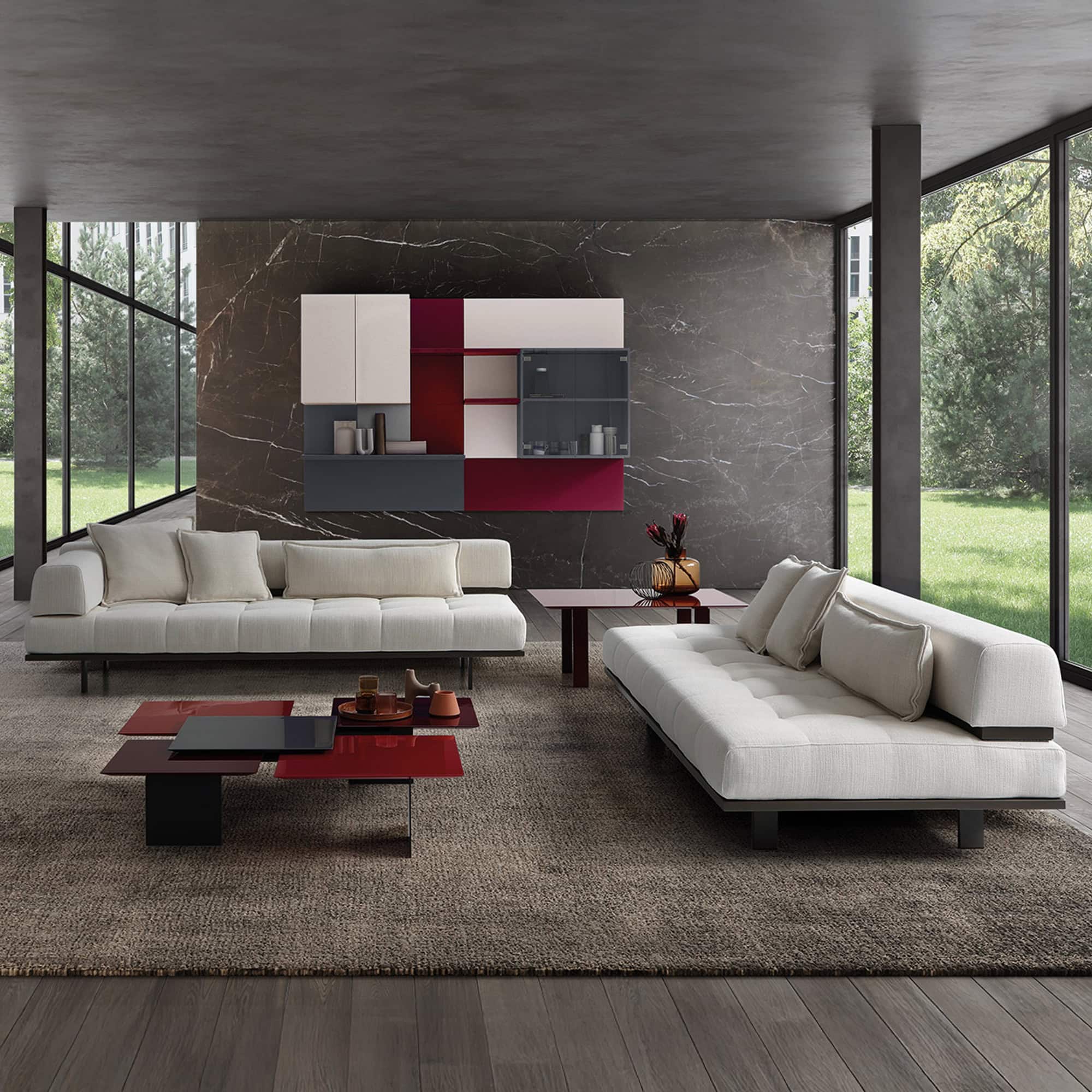 Modern living room with sleek white sofas, bold red, black, and white storage walls, and floor-to-ceiling windows overlooking greenery.