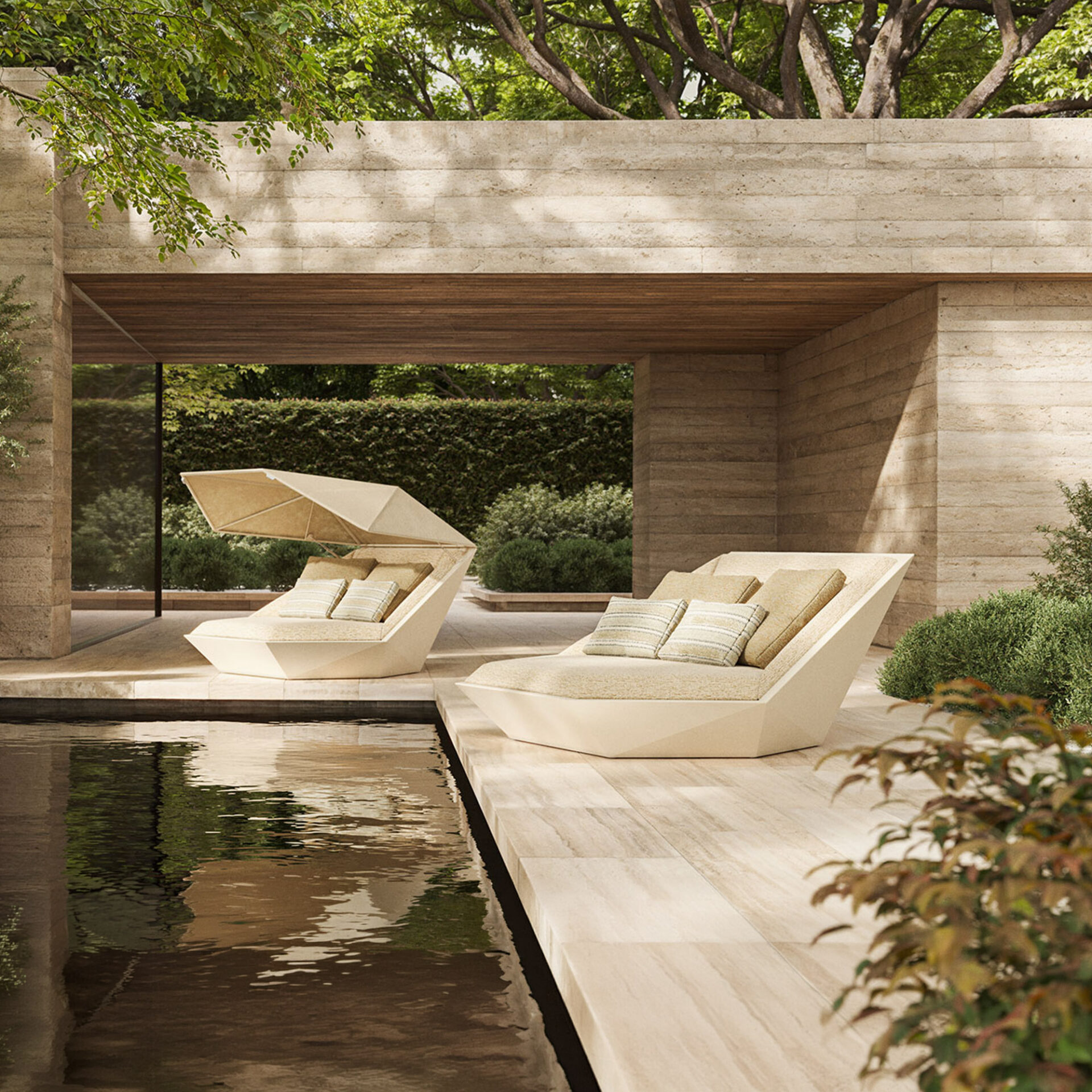 Two modern, geometric beige lounge chairs with cushions sit beside a dark pool on a light tiled deck. The chairs are under a stone and wood architectural overhang, surrounded by lush green trees and bushes.