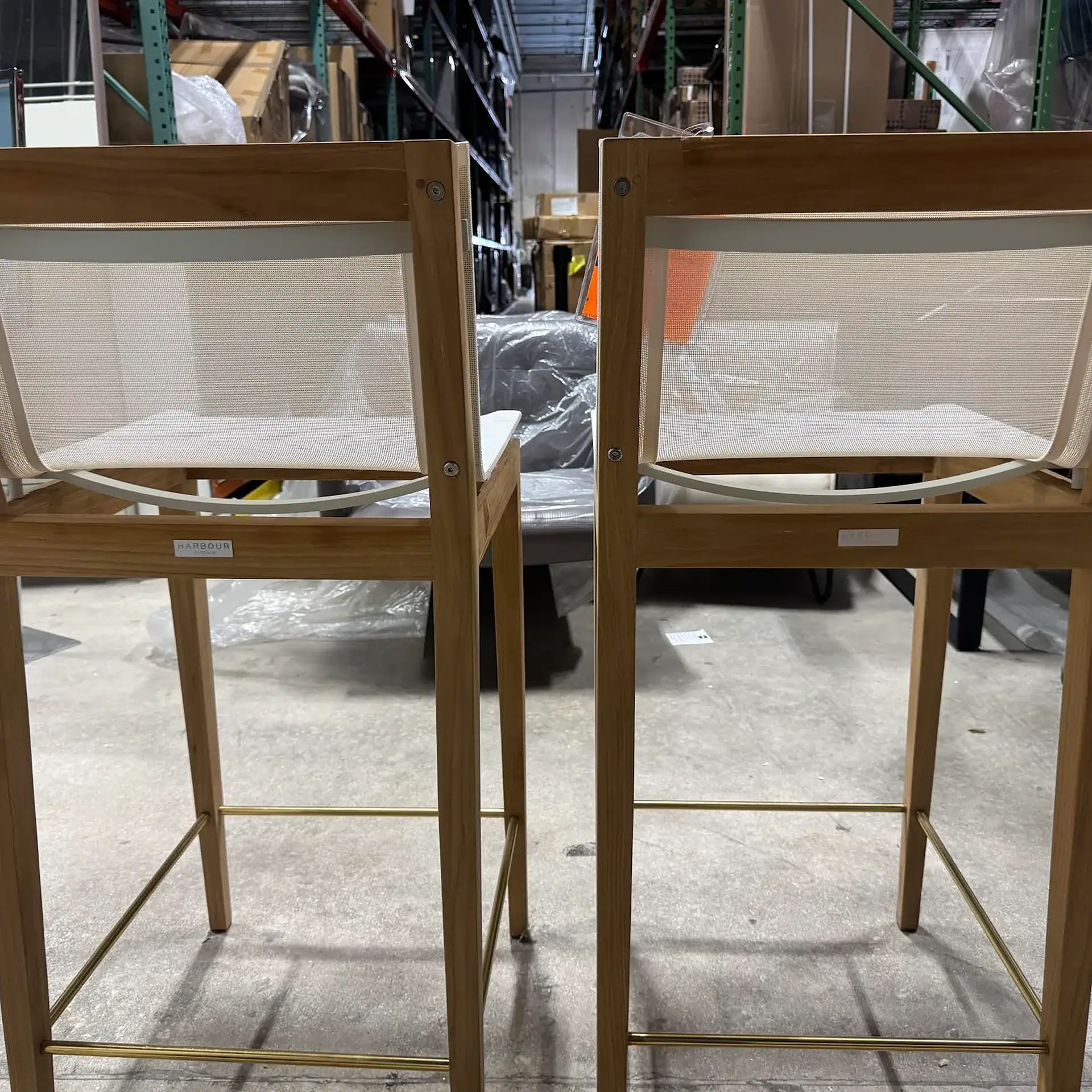 Two Harbour Byron outdoor bar stools with wooden frames and mesh seats in a warehouse.