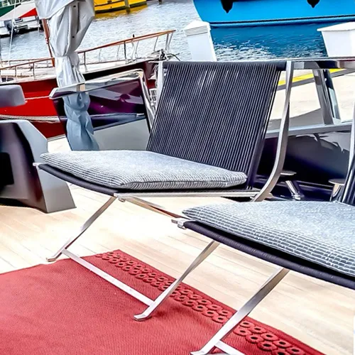 Two modern outdoor chairs with striped cushions on a wooden deck, overlooking a marina with several boats.