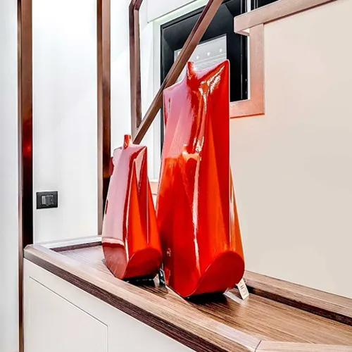 Two glossy, red, abstract decorative objects on a dark wooden shelf against a light wall.