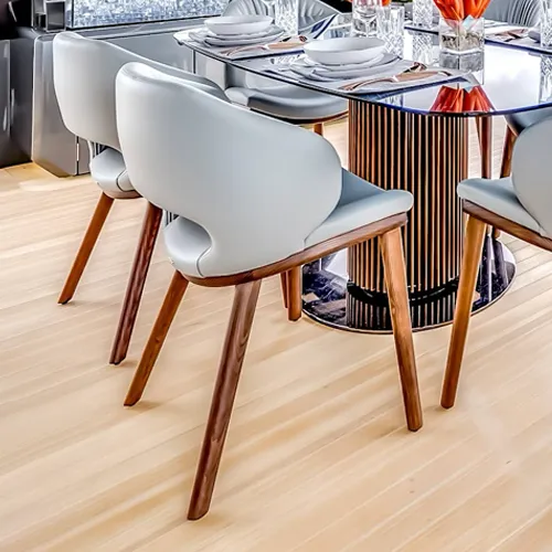 Three light grey modern dining chairs with wooden legs around a glass-top dining table with a metallic slatted base, set with white plates and glasses on a light wood floor.