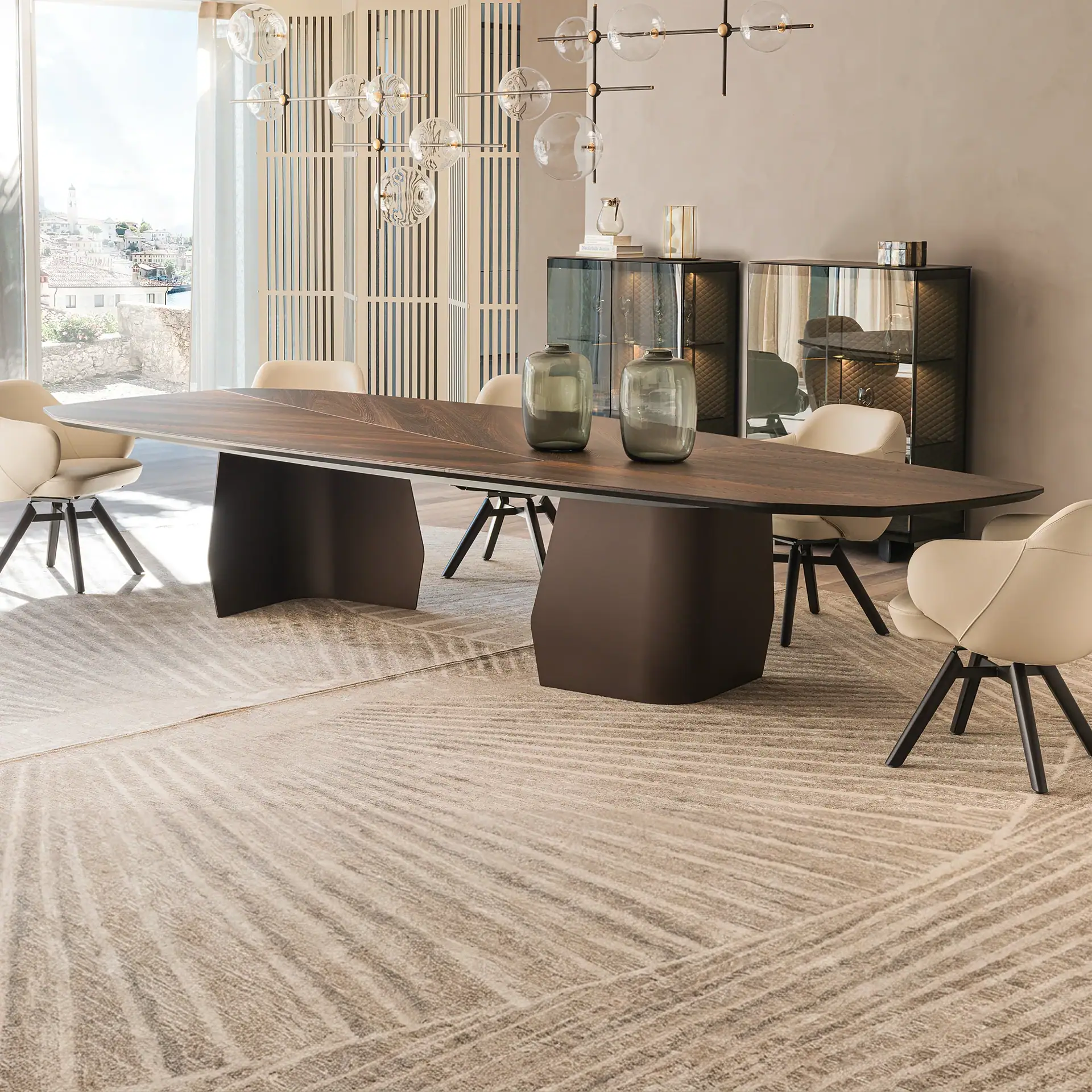 A modern dining room with a dark wood oval table, light beige upholstered chairs, a contemporary glass sphere chandelier, and a large window overlooking a European town.