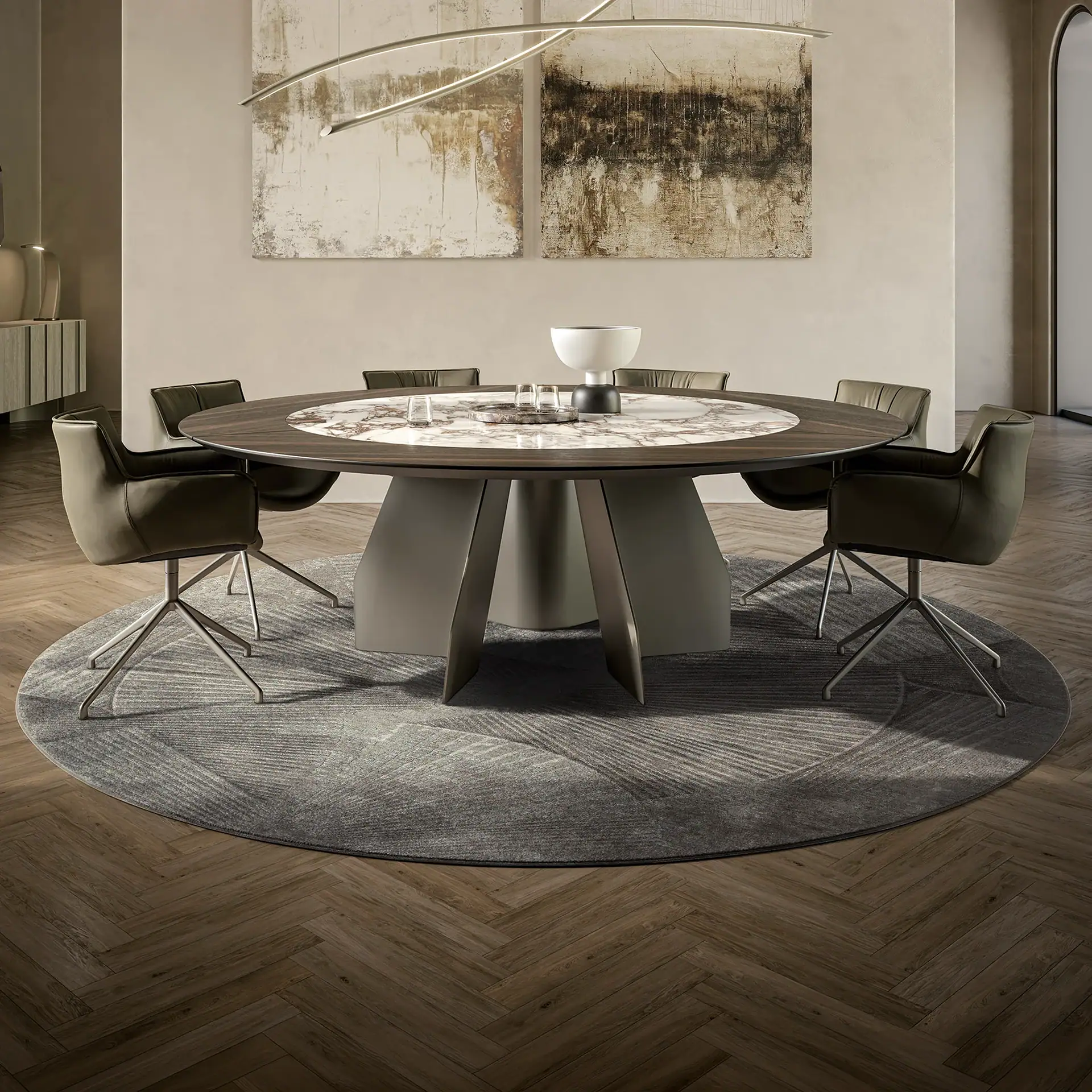 A modern dining room with a round dark wood and marble table, six olive-green chairs, a circular grey rug, and abstract art on light beige walls.