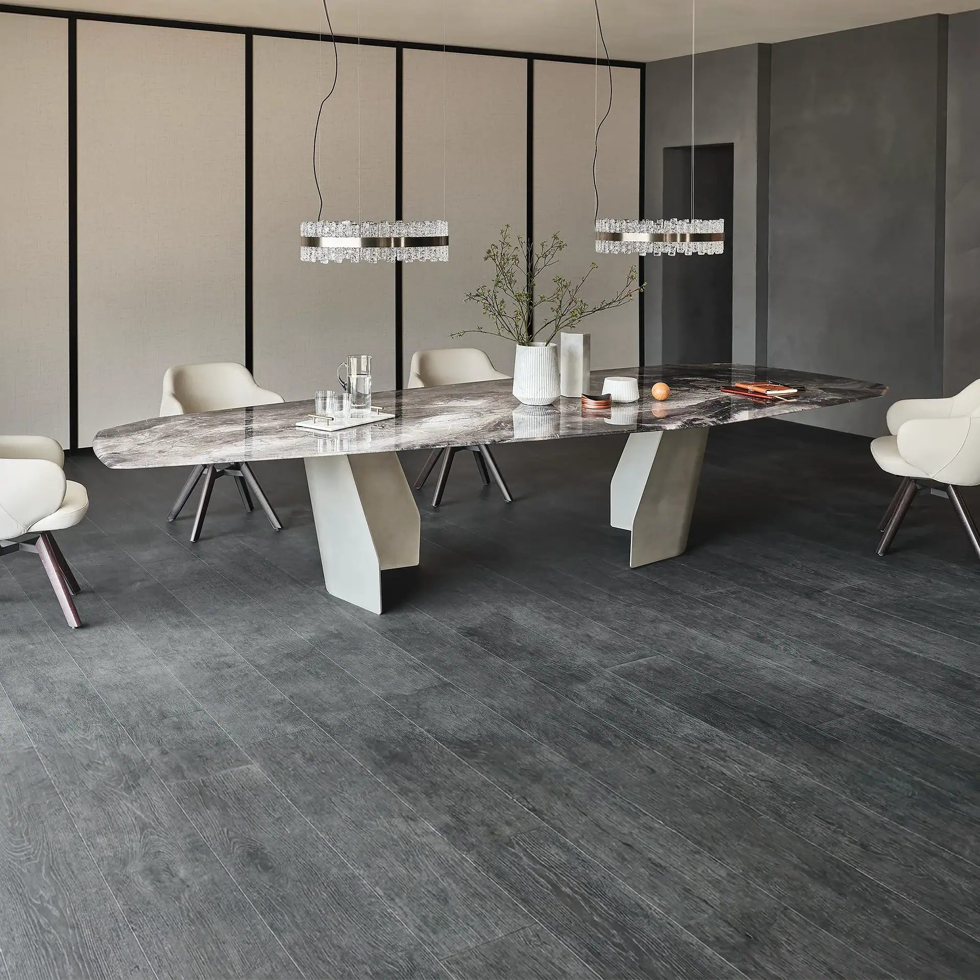 A modern dining room with an oval marble table, cream chairs, and two crystal pendant lights. The room has dark grey textured walls and light beige paneling.