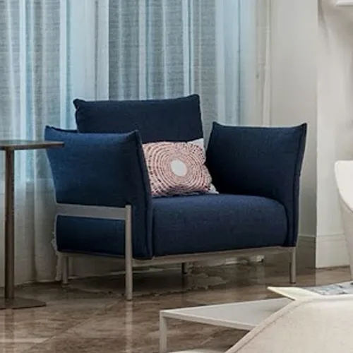 A dark blue armchair with a patterned pillow sits in a modern room next to a side table.