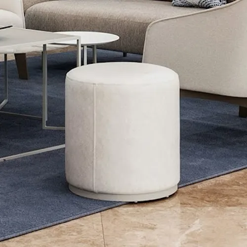 A cream-colored cylindrical ottoman on a dark blue rug in a modern living room setting, with a coffee table and sofa visible.