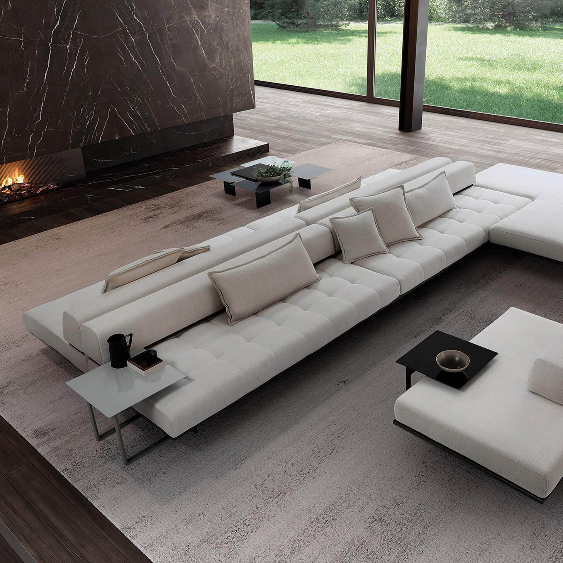 A luxurious modern living room with a large L-shaped cream sectional sofa, a dark marble fireplace with a fire, and floor-to-ceiling windows overlooking a green lawn.