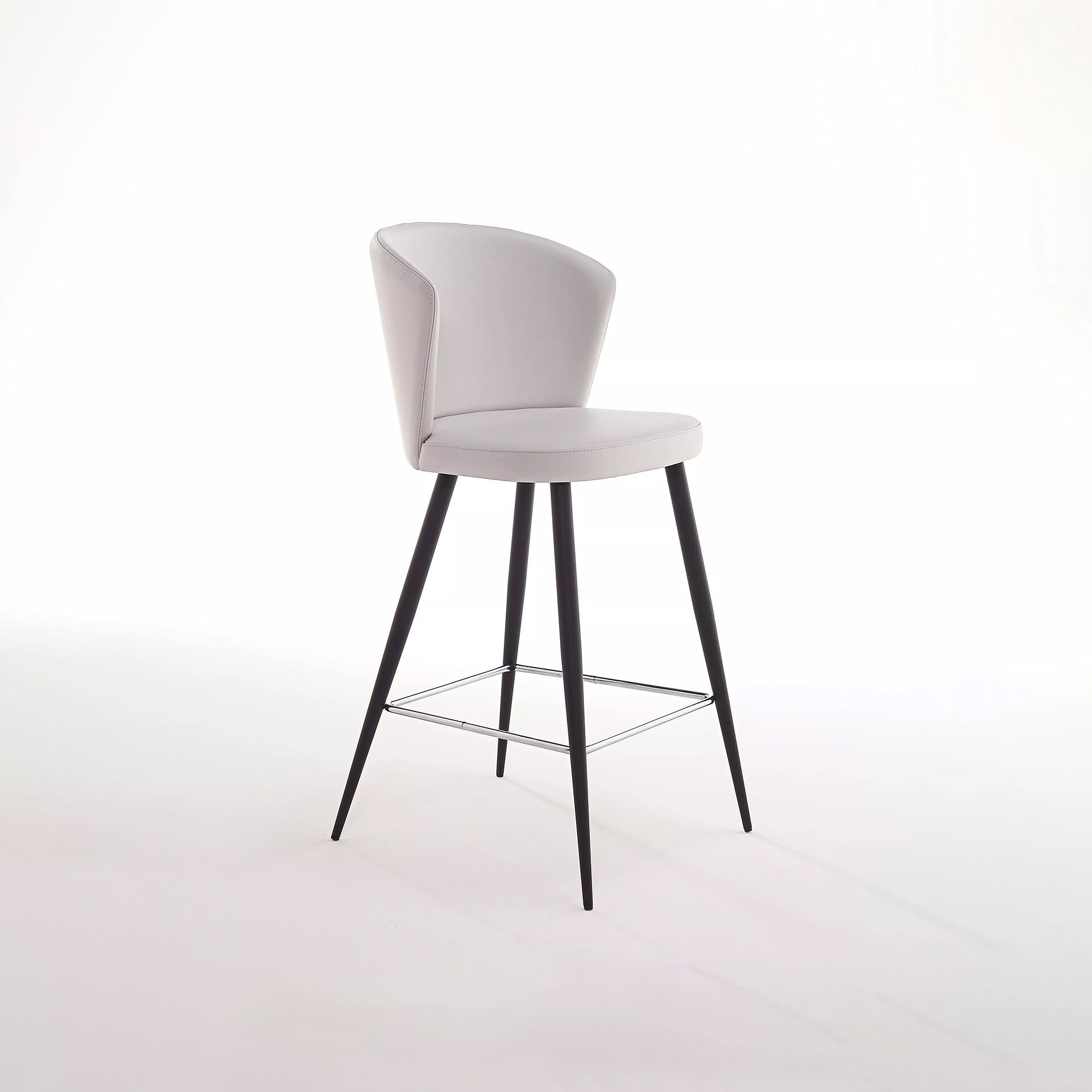 A modern light grey bar stool with a curved backrest, black splayed legs, and a square chrome footrest, set against a white background.