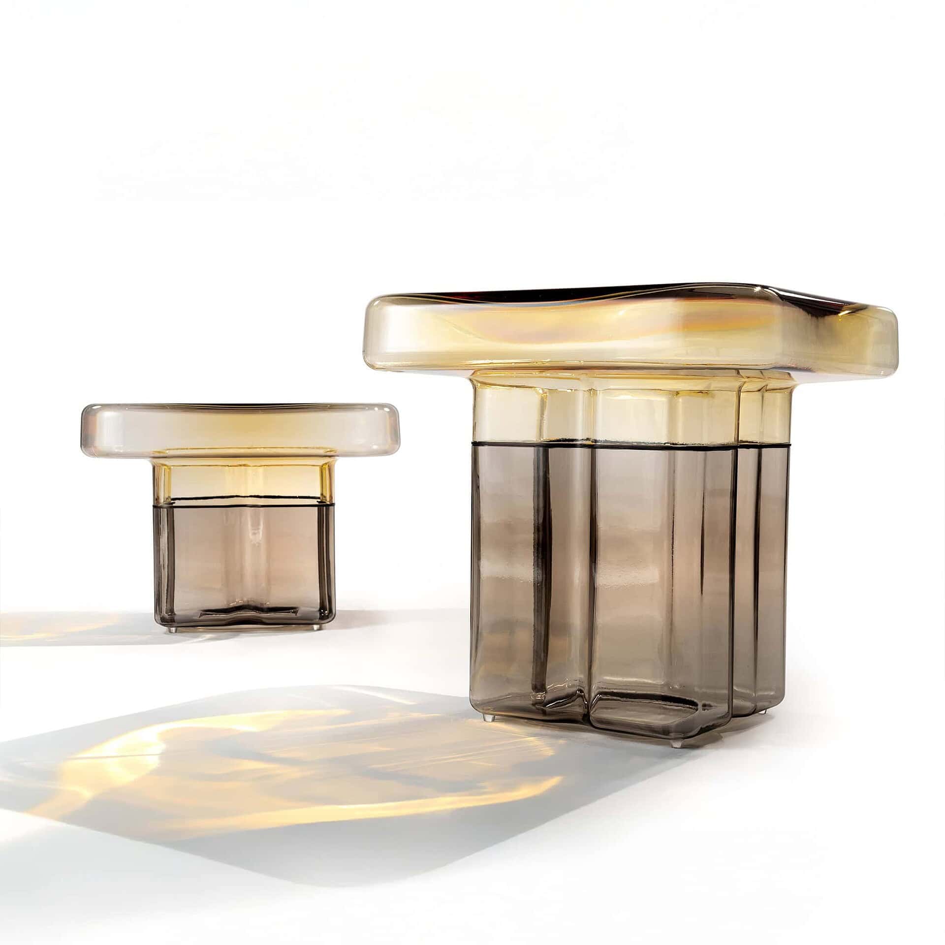 Two T-shaped glass decorative objects on a white background. The larger one is on the right, the smaller on the left. Both have amber tops and smoky grey, fluted bases.